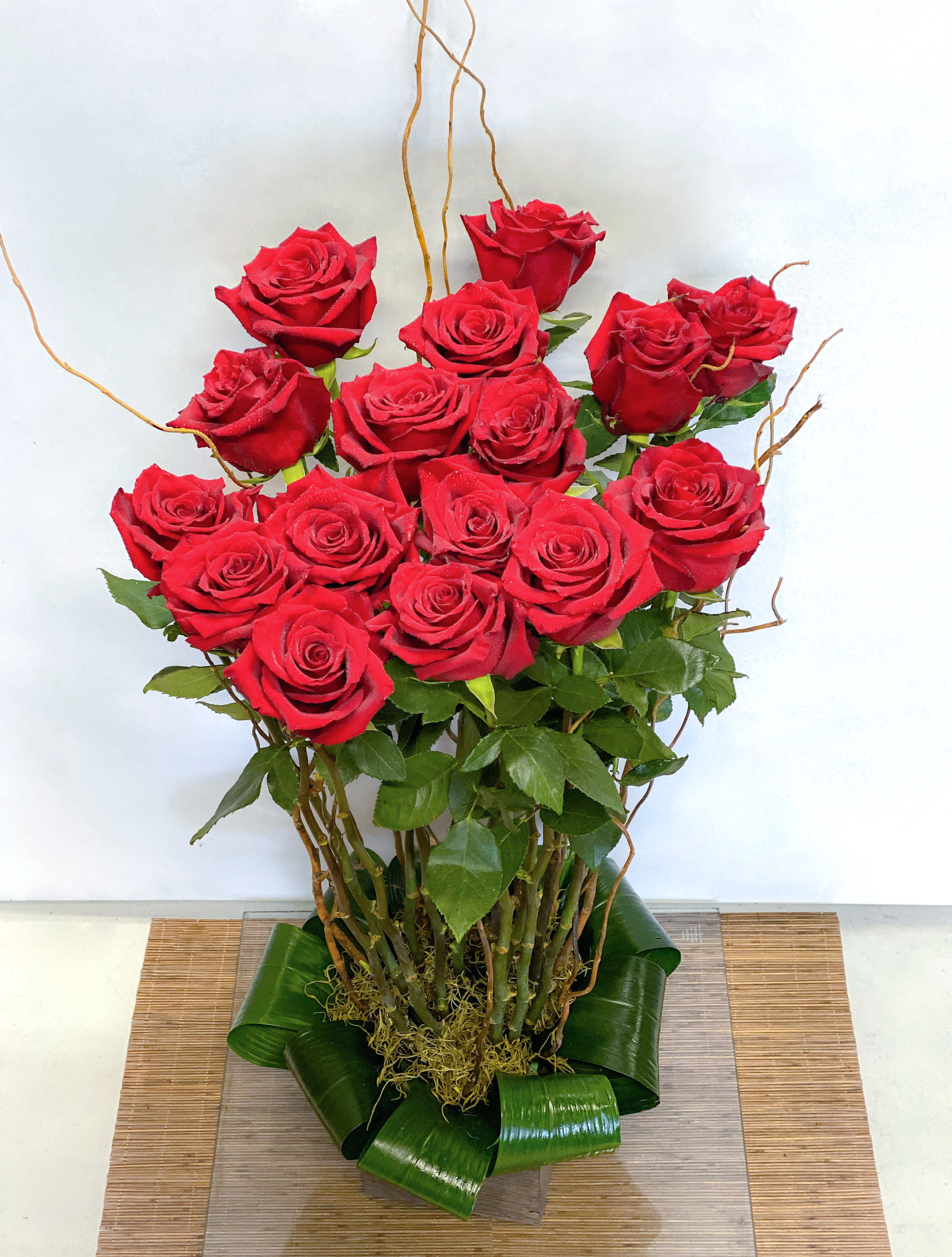 Tall bouquet of red roses with green leaves and decorative twigs