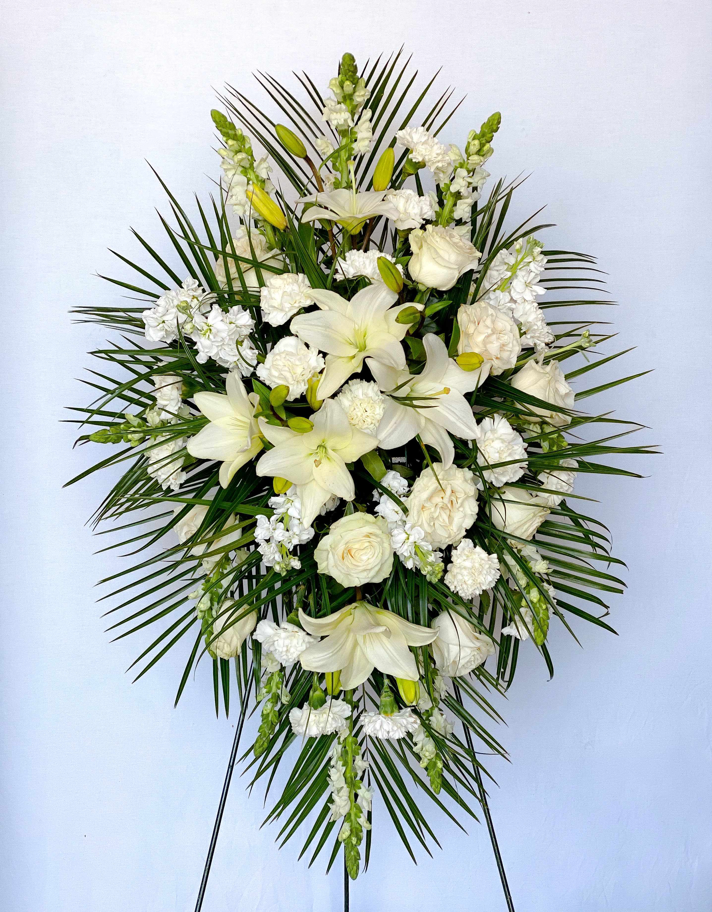 White floral standing spray with lilies and roses on a palm backdrop