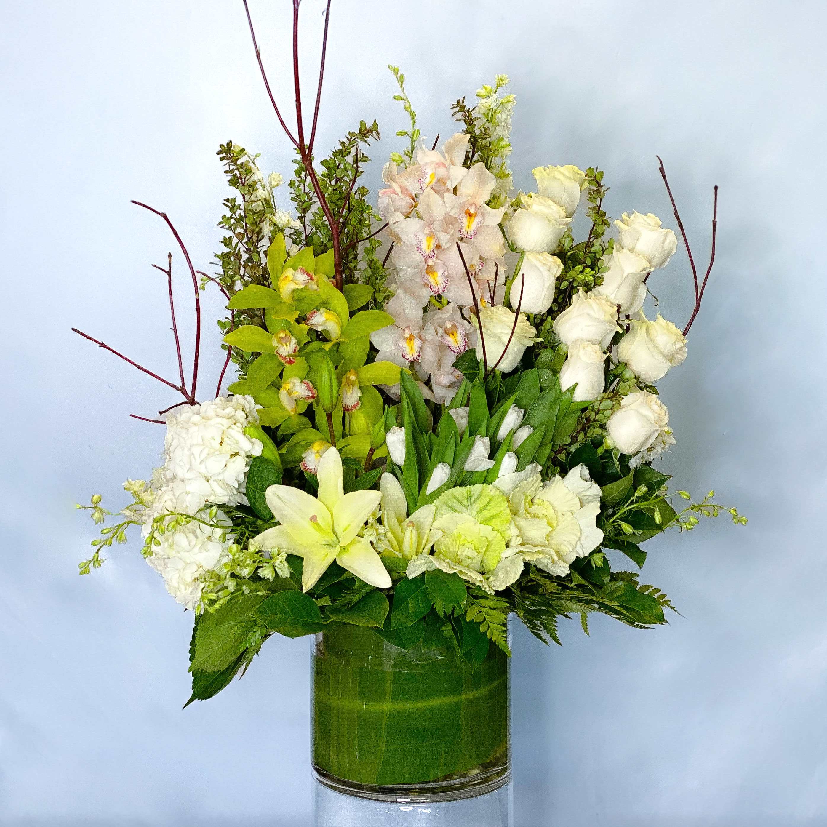 White roses, orchids, and lilies arranged in a green glass vase