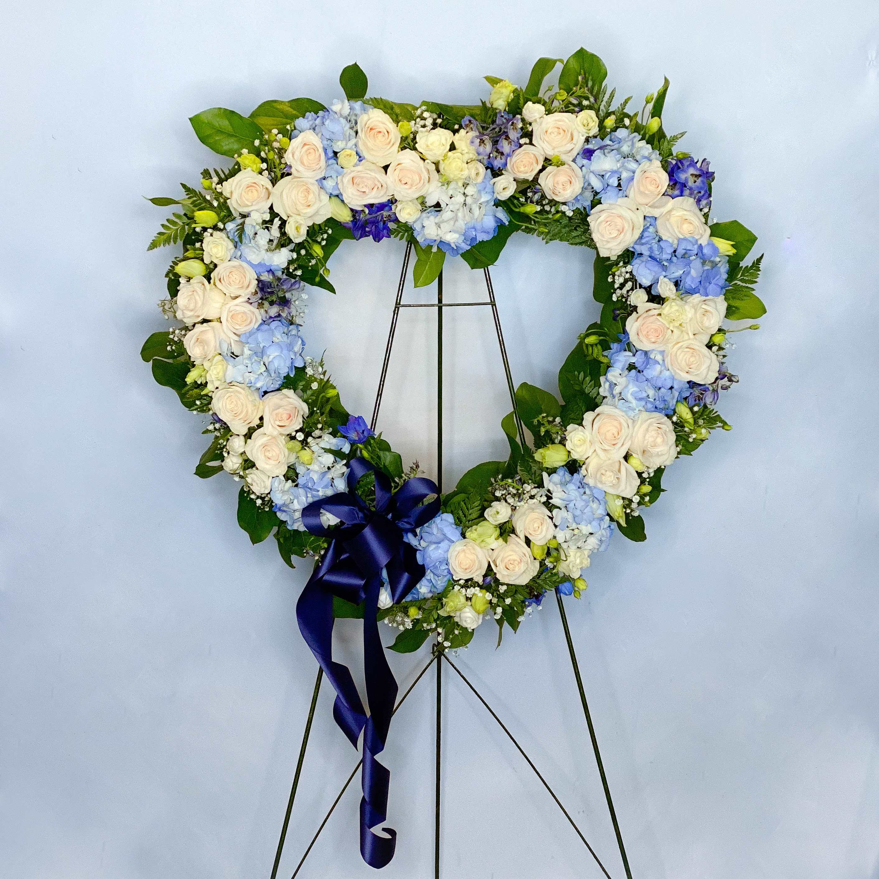 Heart-shaped floral wreath with white and blue flowers on a stand