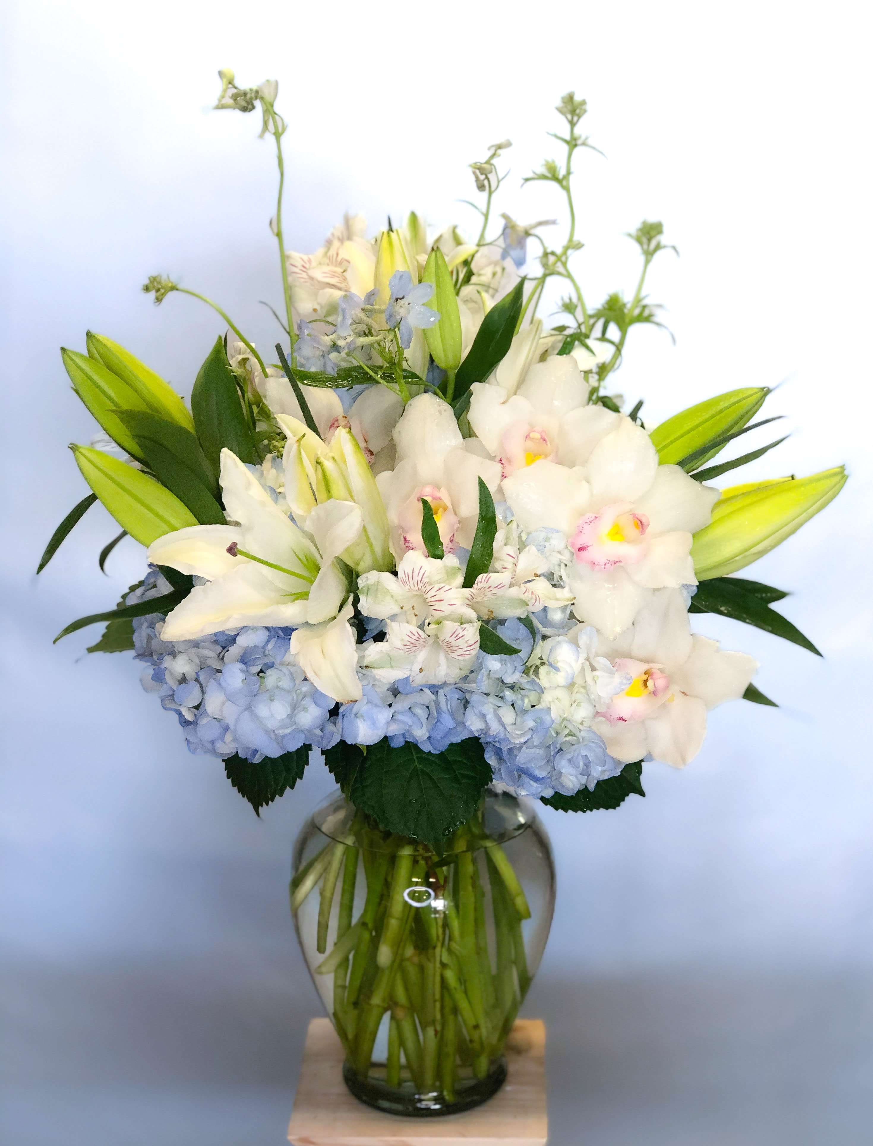 White lilies and orchids in a glass vase with blue hydrangeas