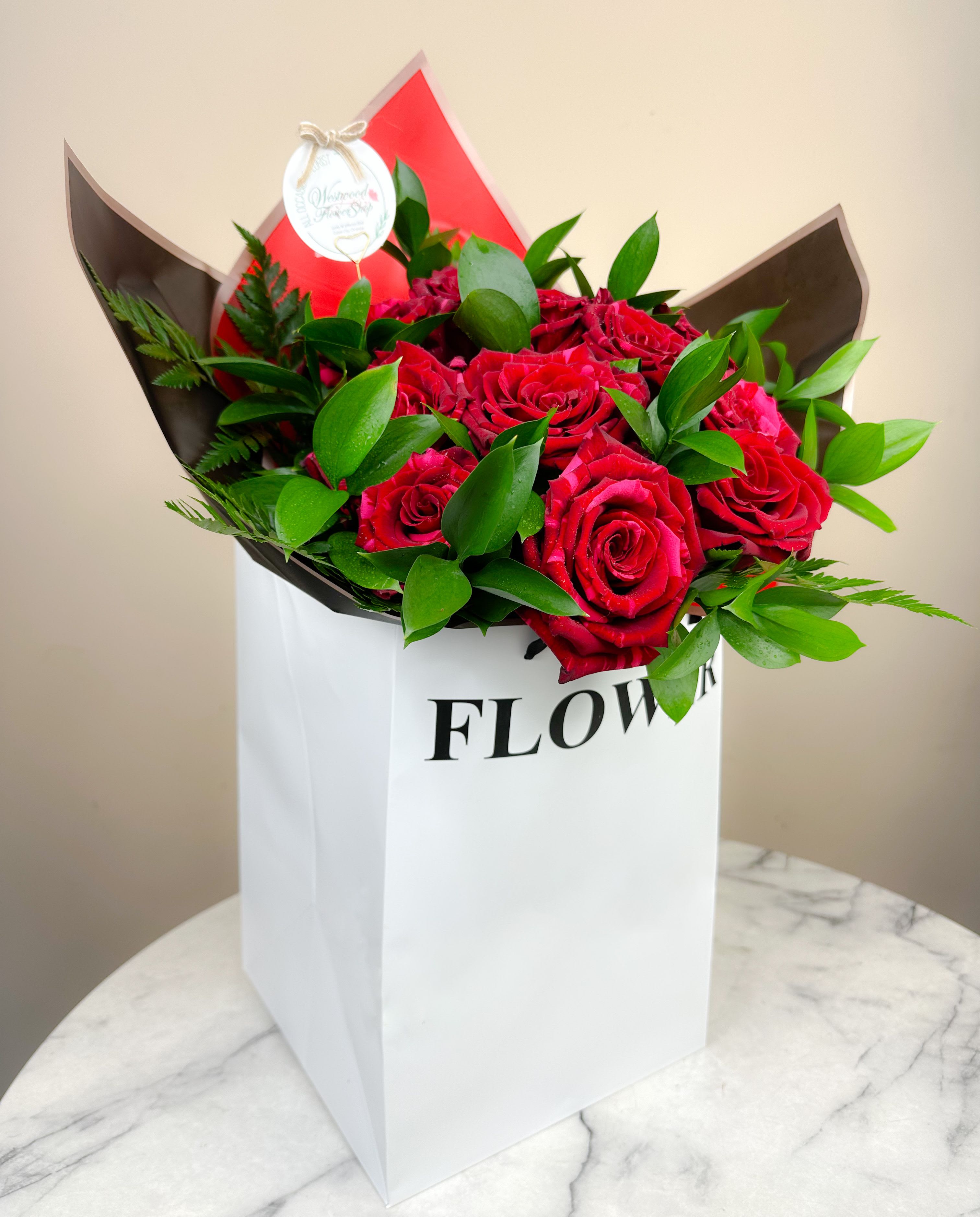 Red roses arranged in a white gift bag with green foliage