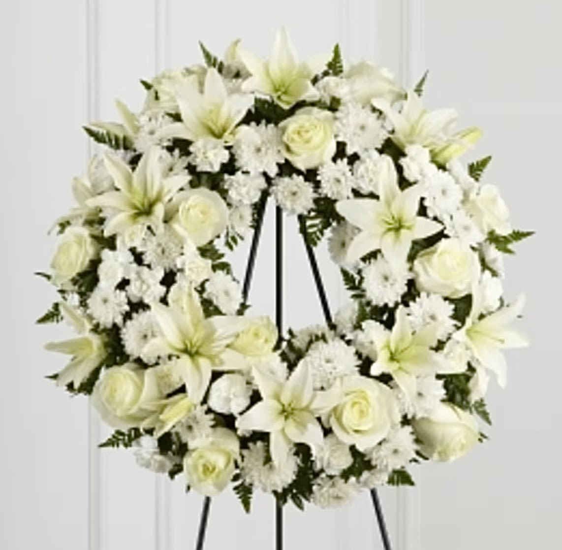 White floral wreath with lilies and roses on a black easel