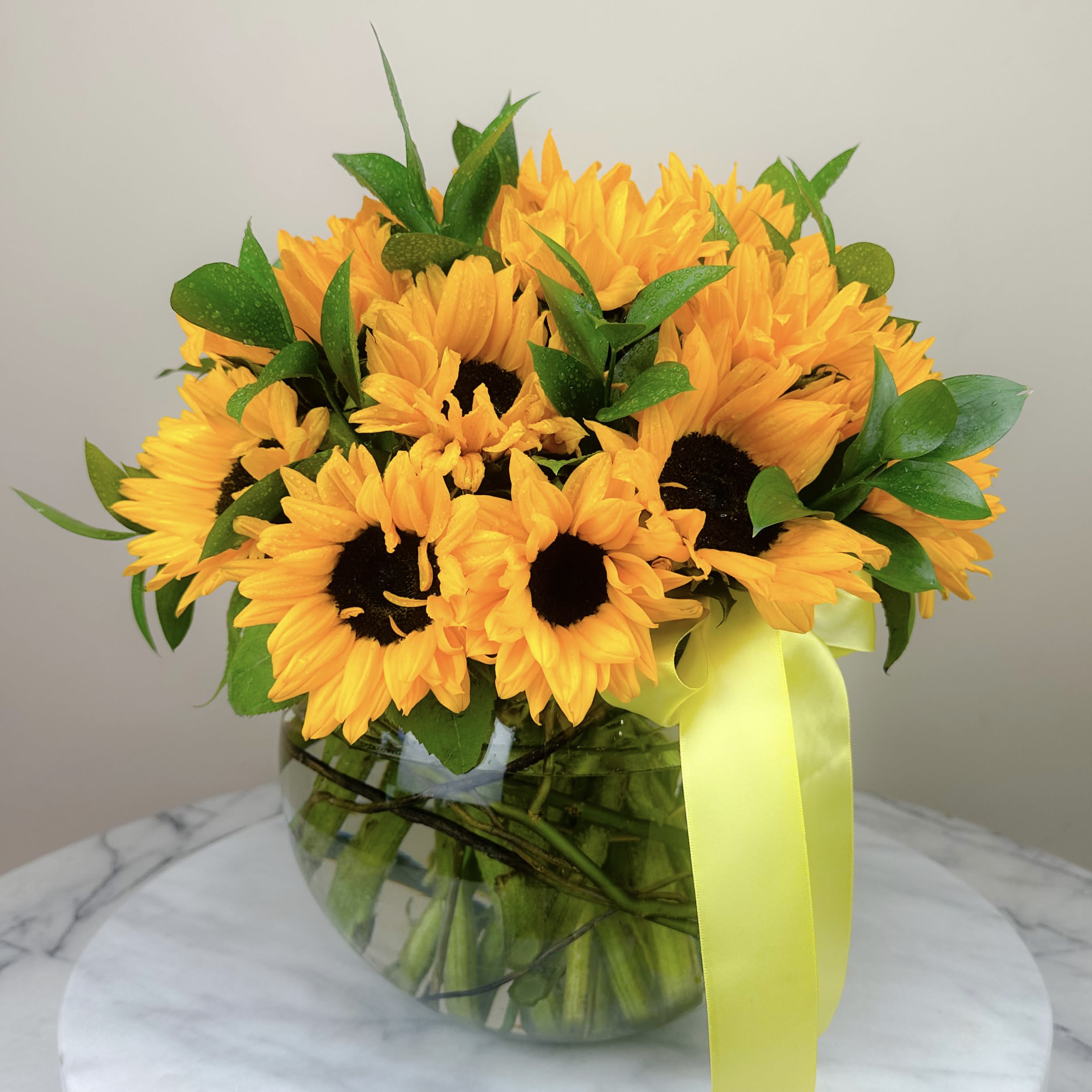 Bouquet of yellow sunflowers in a glass vase with a yellow ribbon