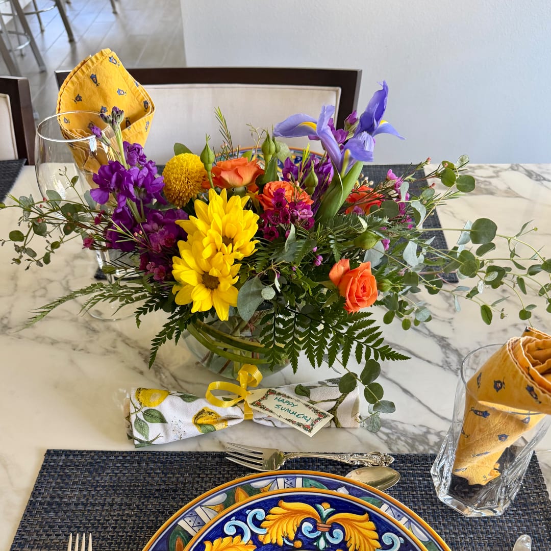 Colorful mixed flower arrangement in a clear glass vase on a dining table