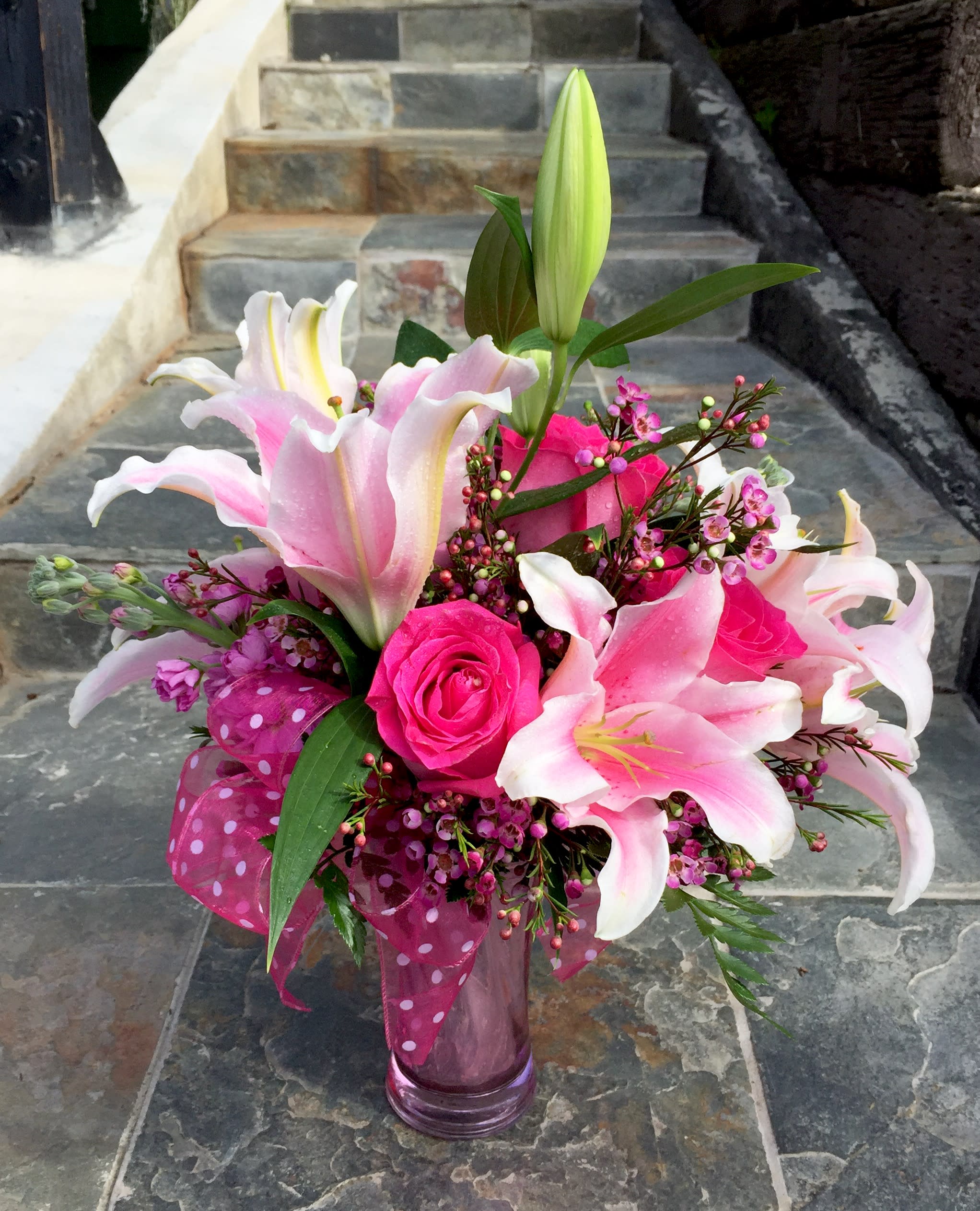 Pink lilies and roses arranged in a glass vase with a polka-dot ribbon.