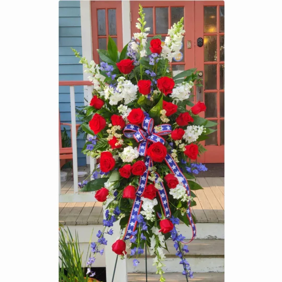 Tall standing floral spray with red roses, white flowers, and blue accents on an easel