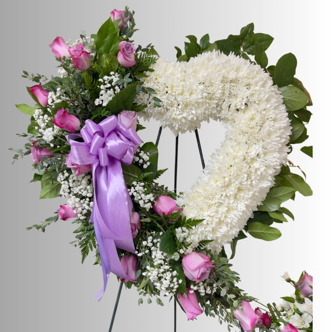 Heart-shaped floral wreath with pink roses and white flowers on a stand