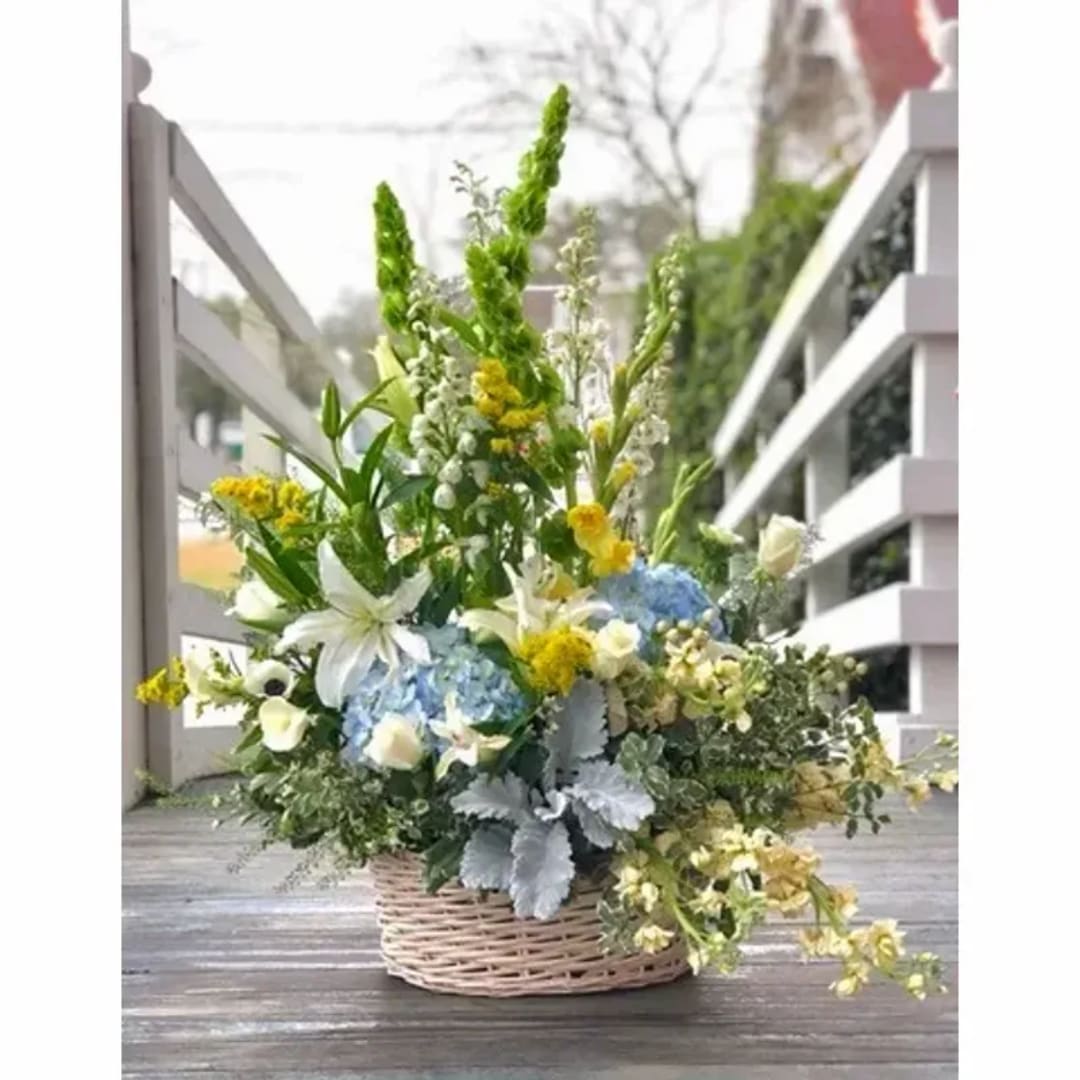 Basket arrangement with white lilies, blue hydrangeas, and yellow flowers