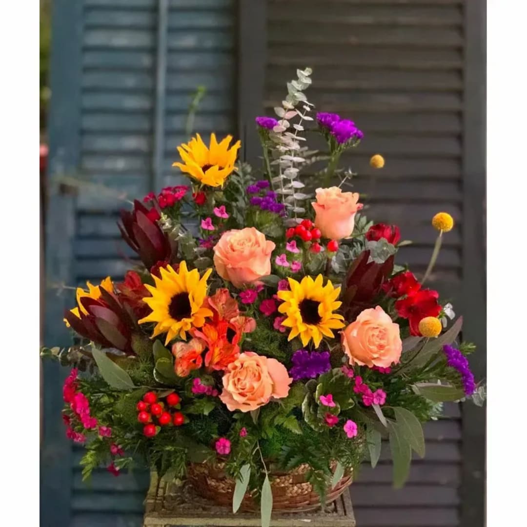 Colorful mixed flower arrangement in a woven basket with sunflowers and peach roses
