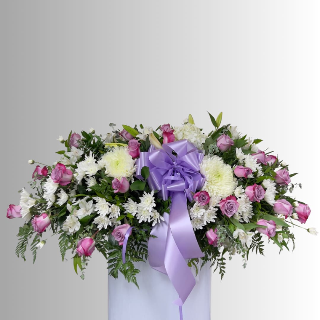 Pink roses and white daisies arranged in a white vase with a lavender ribbon