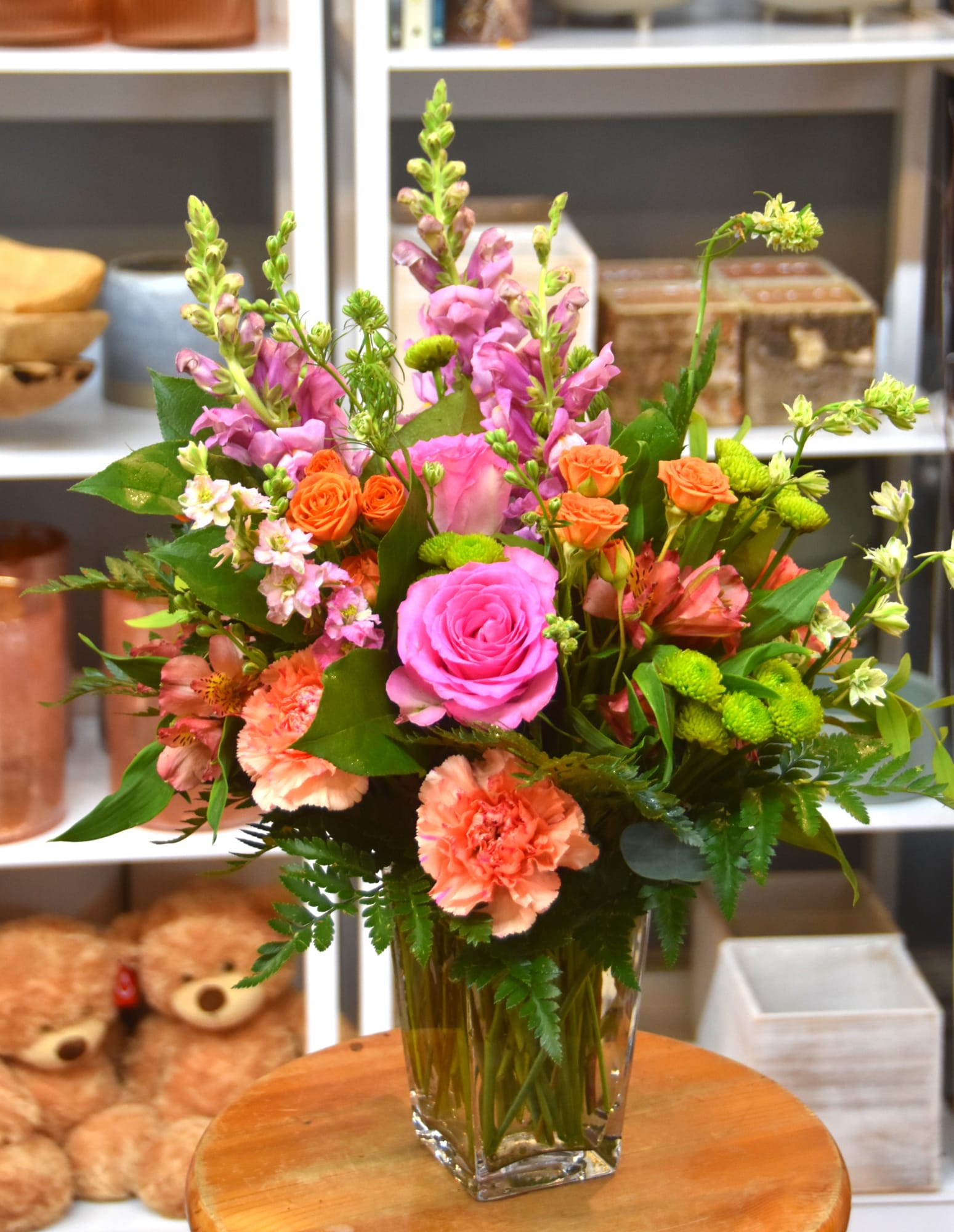 Tall mixed bouquet with pink roses, peach carnations, and orange spray roses in a clear glass vase