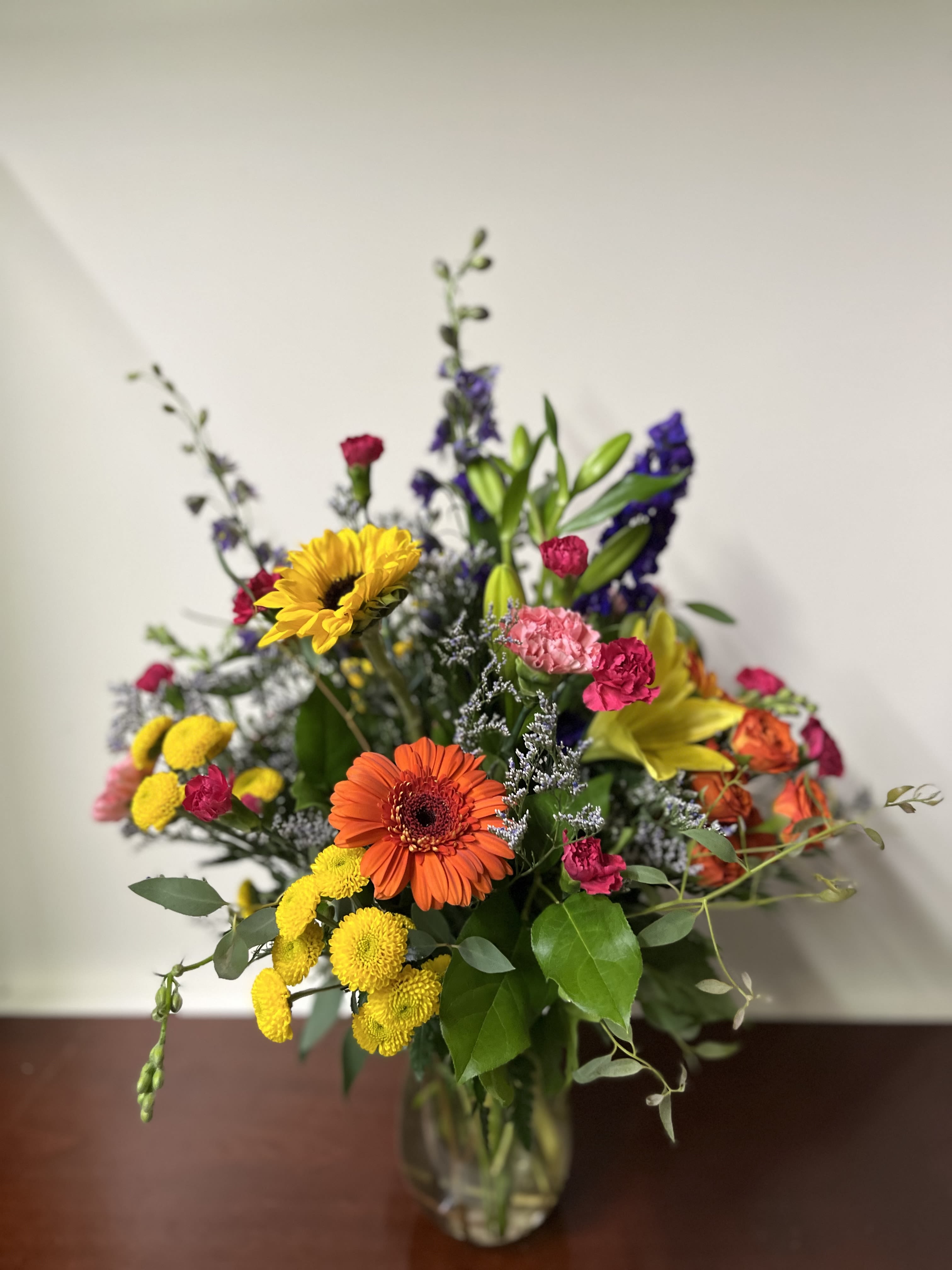 Mixed bouquet in a glass vase with sunflowers, gerbera daisies, and colorful blooms
