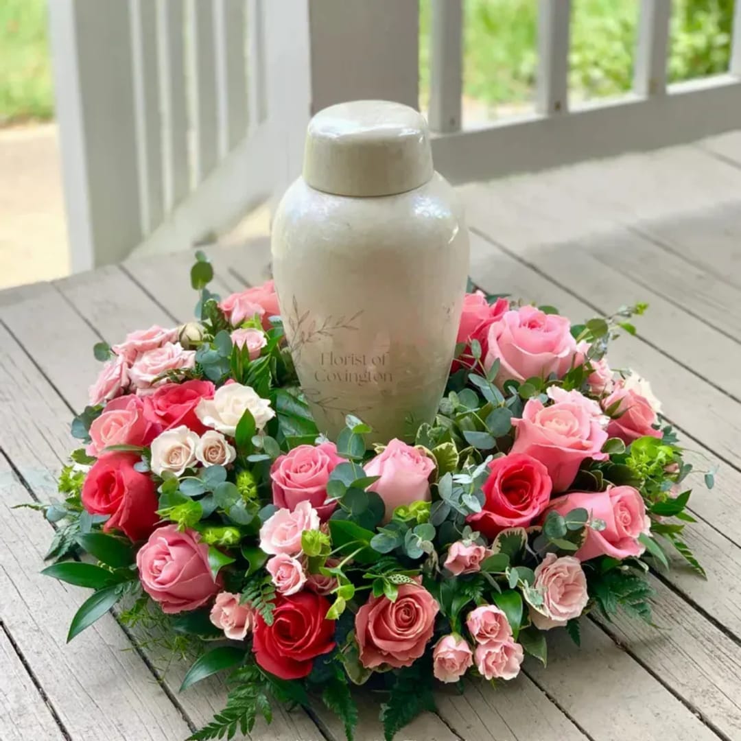 Pink and red rose wreath around a white urn on a wooden table