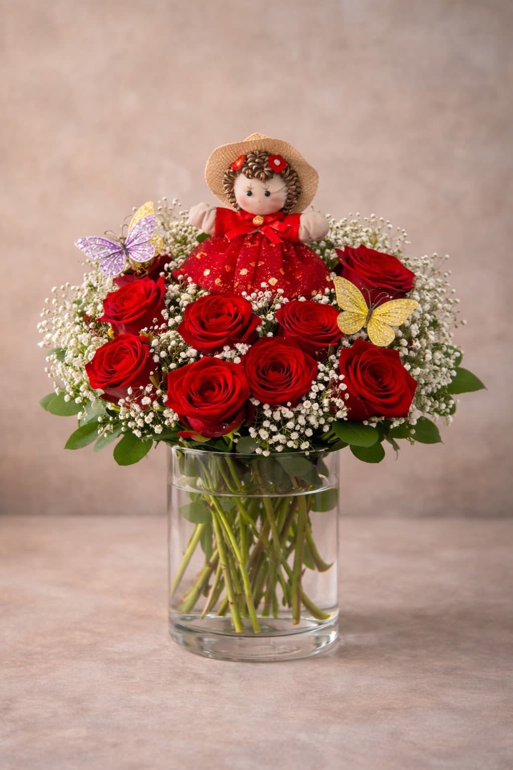 Amorcito Garden Vase 12 Roses - A romantic arrangement of fresh roses accented with delicate butterflies and a charming decorative figure. Sweet, unique, and unforgettable — a Valentine’s gift that feels personal and heartfelt. Each arrangement includes one decorative doll figure placed within the design to create a playful, boutique-style look. Doll style and colors are selected at random based on availability. Every arrangement is handcrafted and one of a kind. Color Doll Meanings • ️ Red Love theme •  Pink Cute theme •  Yellow Friendship theme •  Lilac Princess theme •  Green Fairy theme