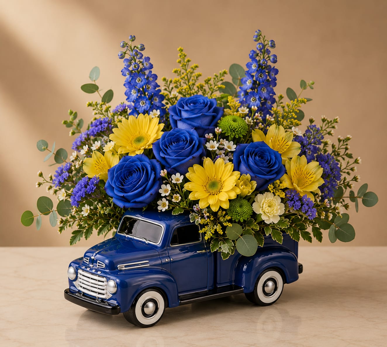 Blue Sapphire Bloom Truck - Bold, vibrant, and unforgettable, Blue Ribbon Dad is designed to celebrate the fathers who always go the extra mile. Arranged in a classic blue pickup truck keepsake vase, this cheerful Father’s Day design features striking blue roses, blue delphinium, sunny yellow daisies, yellow alstroemeria, statice, green button poms, wax flower, eucalyptus, and seasonal greenery.  The combination of rich blues and bright yellows creates a powerful expression of admiration, loyalty, friendship, and gratitude. The keepsake truck vase adds a nostalgic touch that Dad can enjoy long after the flowers have bloomed.  Perfect for Father’s Day, birthdays, retirement celebrations, or simply showing appreciation for the special men in your life.