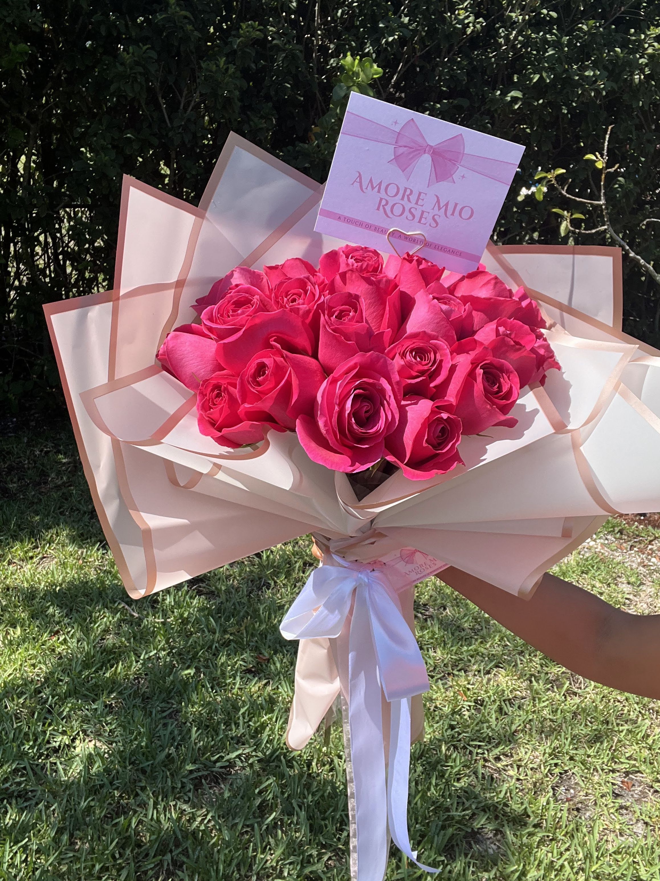 Bouquet of bright pink roses wrapped in blush paper with a white ribbon