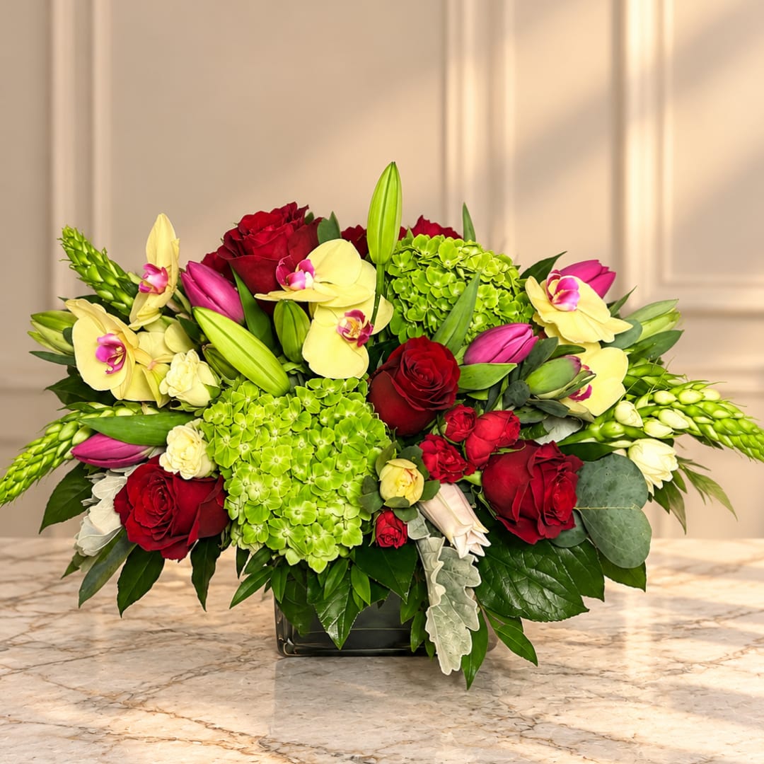 Mixed bouquet of red roses, green hydrangeas, and yellow orchids in a black vase