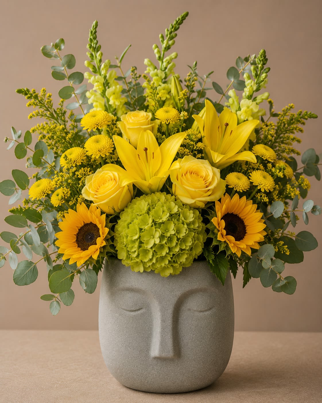 Golden Radiance Face Planter - Bright, bold, and full of warmth, Golden Tribute for Dad is a cheerful Father’s Day arrangement designed to celebrate the strength, guidance, and love that fathers bring into our lives. Featuring radiant sunflowers, sunny yellow roses, vibrant yellow lilies, green hydrangea, yellow button poms, golden solidago, snapdragons, and fresh eucalyptus, this design creates a striking display of color and texture.  Arranged in a modern gray face vase, this cheerful garden-inspired design symbolizes happiness, gratitude, optimism, and admiration. It’s the perfect gift for dads who bring sunshine into every day and deserve to be celebrated in a memorable way.