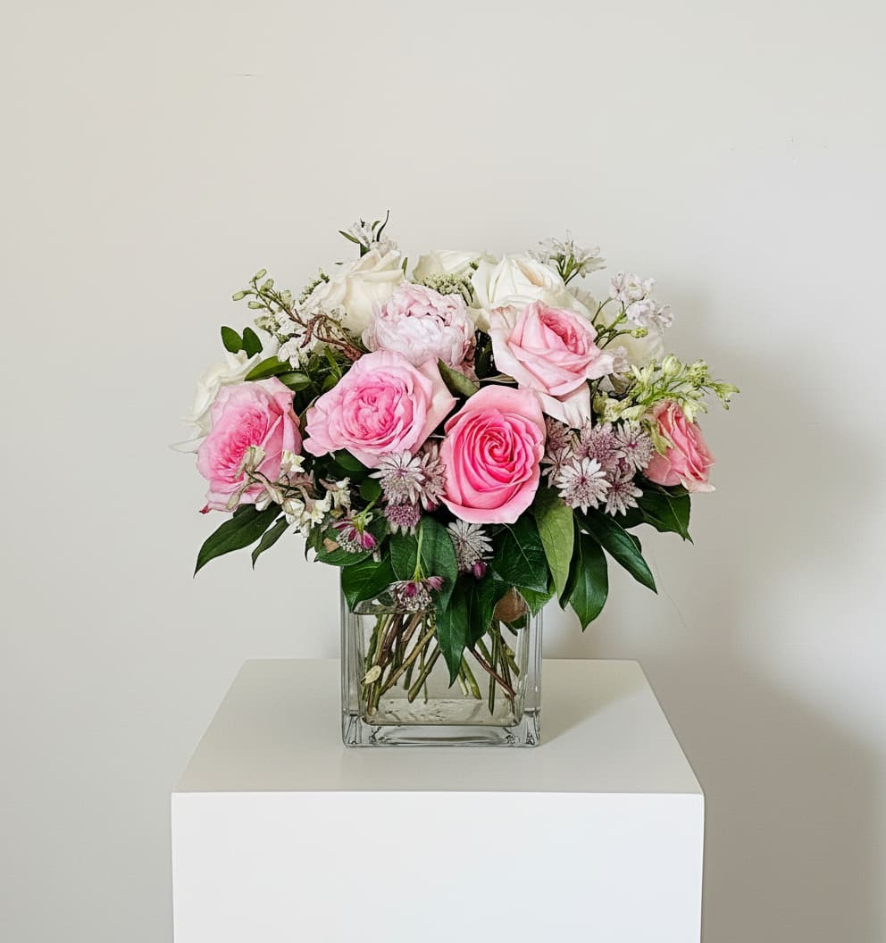 Pink and white roses arranged in a clear square vase