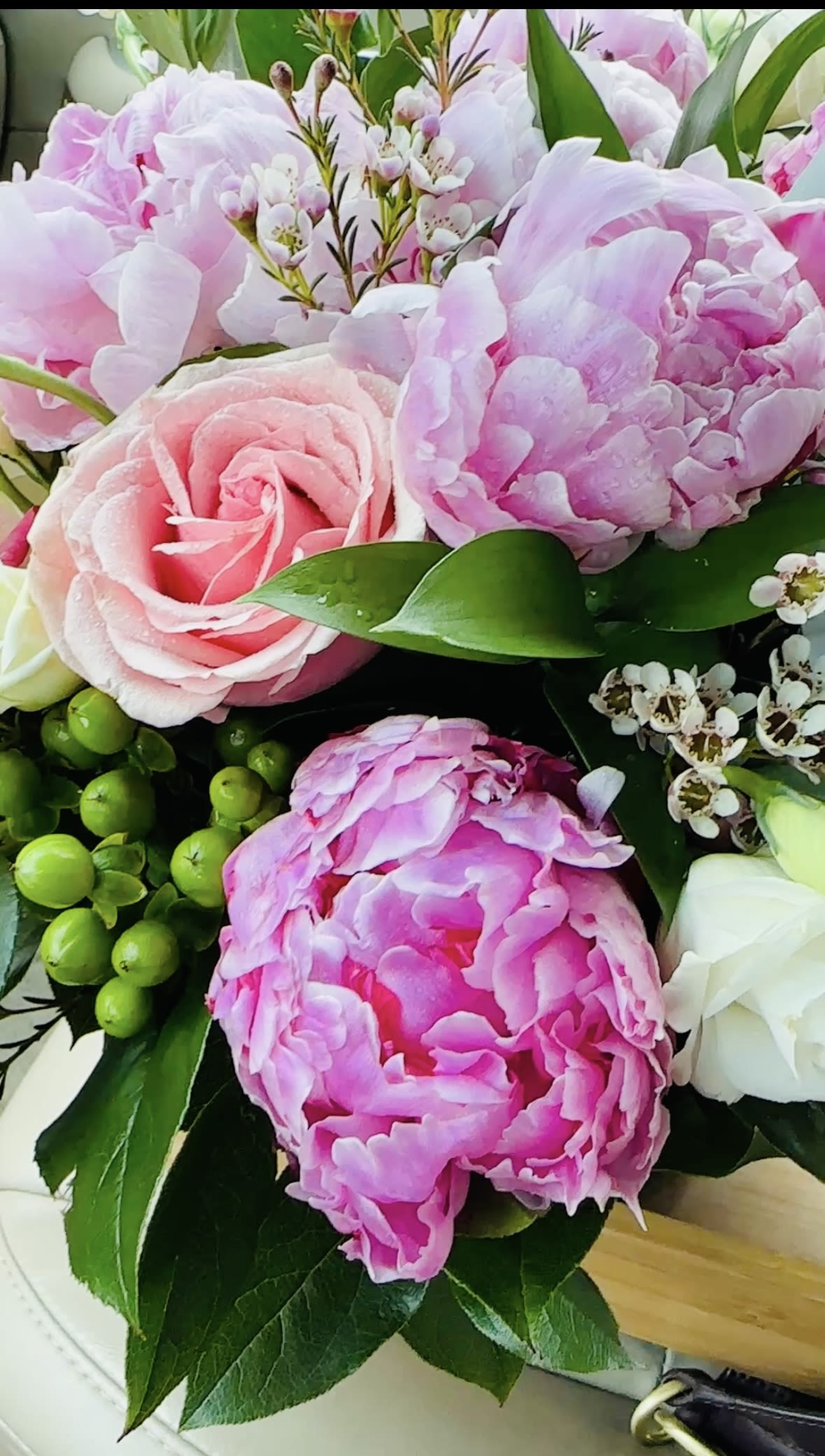English Garden Arrangement ( Peony, Roses, Garden Roses) - Ruffled pink peonies and soft blush roses create an immediately romantic, feminine impression in this English Garden arrangement-perfect as a birthday bouquet, a spring surprise, or a thoughtful get well gift for the person you're thinking of. The full, closely grouped blossoms read like a hug in flowers: she'll feel genuinely celebrated and cared for the moment this mix of roses and peonies arrives.  This arrangement pairs peonies, garden roses, and spray roses with white stock and delicate lisianthus touches, accented by glossy green berries and small white filler blooms for texture and contrast. Presented in a wooden container with a leather strap and metal buckle, it has a charming, hand-carried look that suits thank you gestures, thinking of you moments, and intimate anniversary or love-and-romance surprises. Colors stay in a soft palette of pink, green, and white to keep the design fresh and wearable year-round. Available for pickup and delivery around Leesburg, VA; the compact, abundant styling makes it easy to display on a bedside table or dining table-lightly mist blooms and keep away from direct heat to help peonies and roses last.
