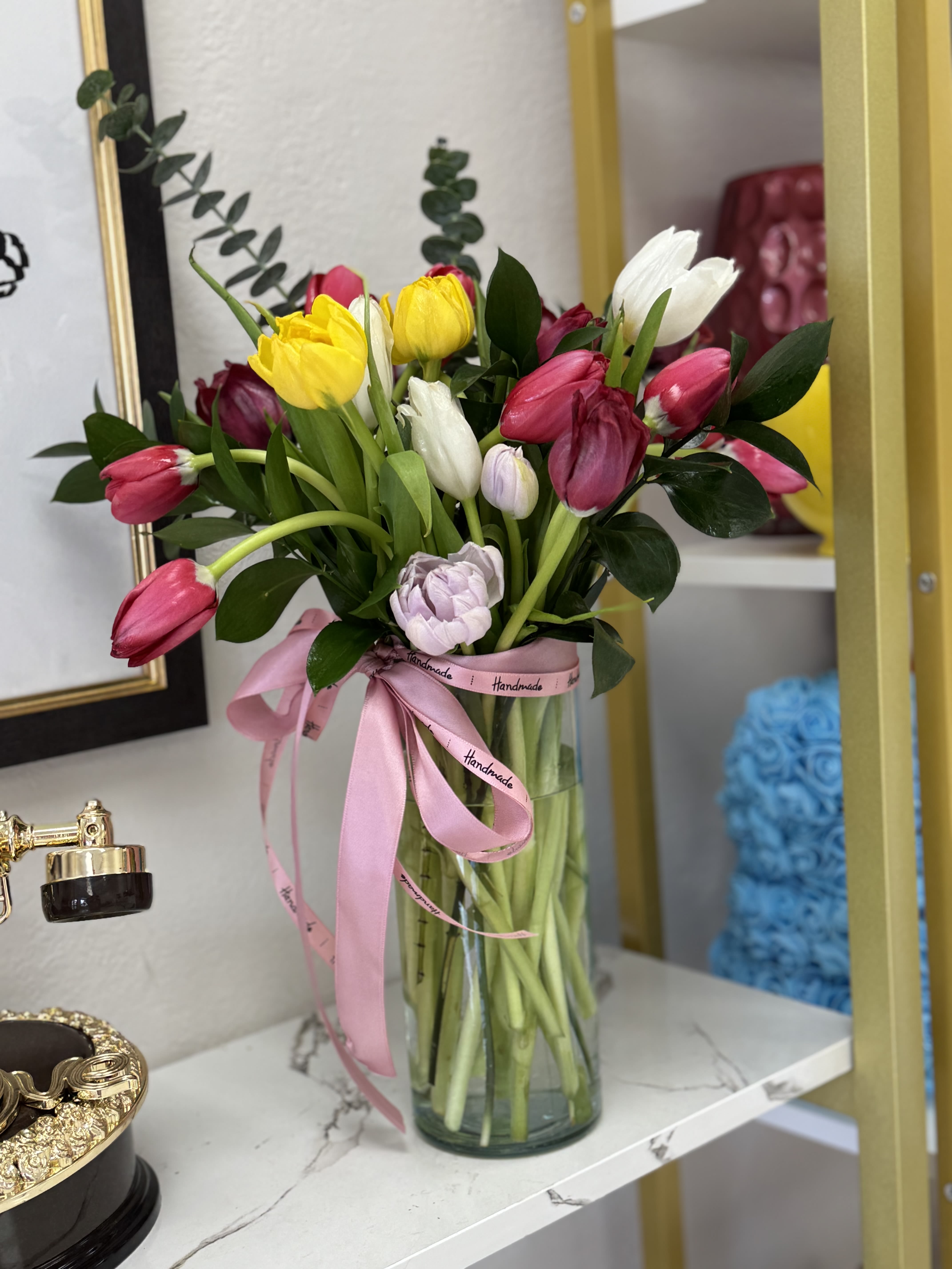 Bouquet of pink, yellow, and white tulips in a glass vase with a pink ribbon