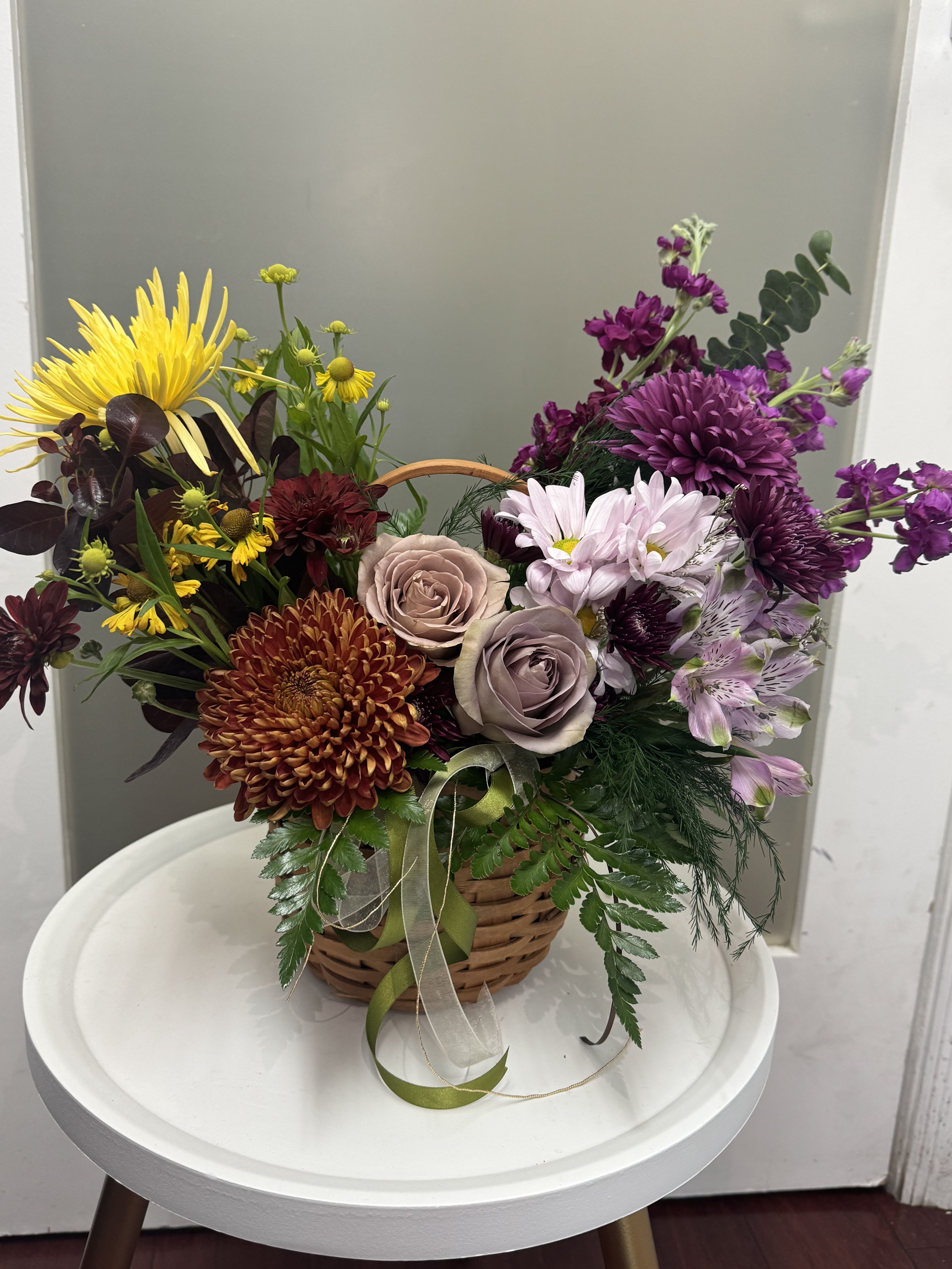 Basket arrangement of mixed flowers in yellow, purple, pink, and burgundy