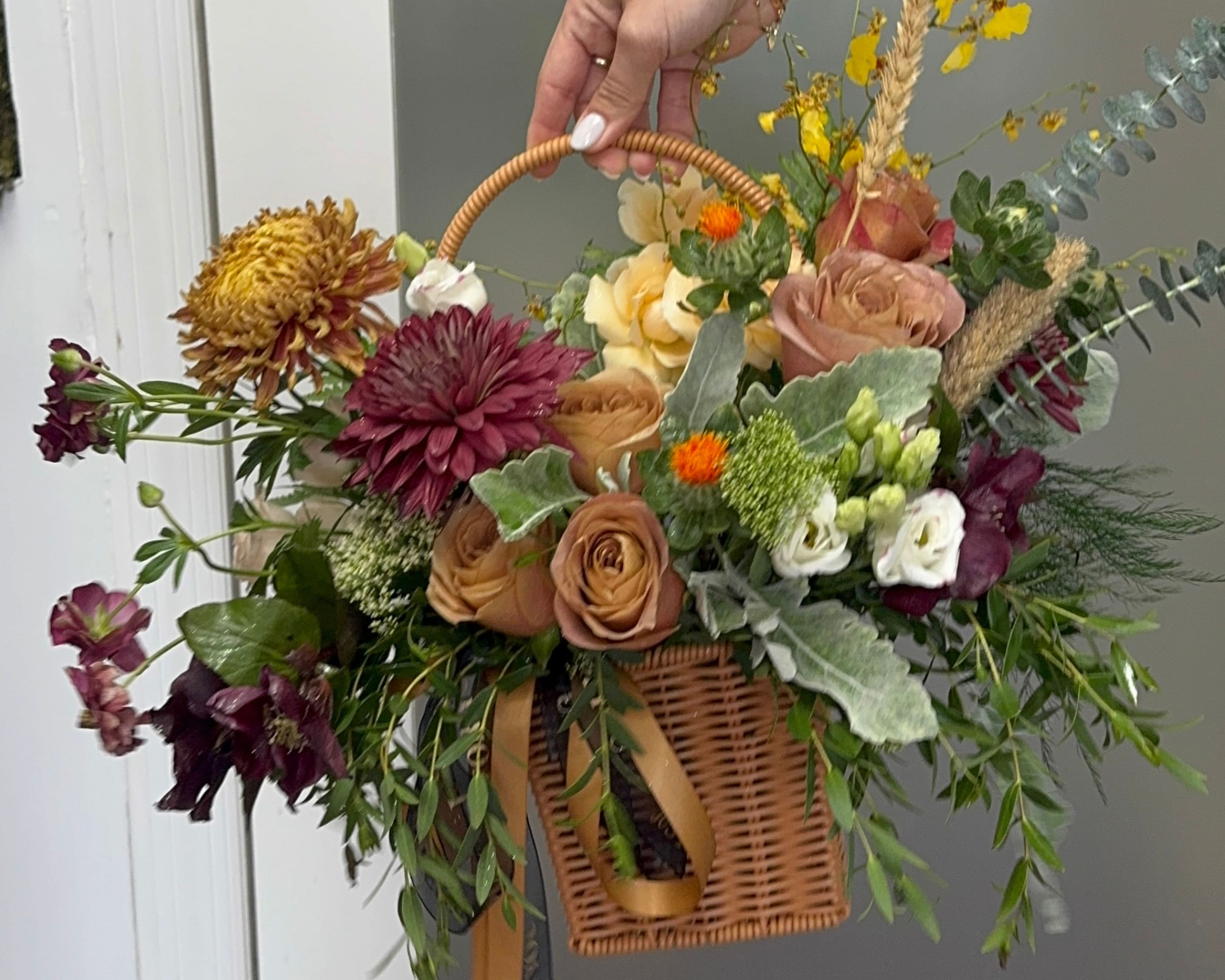 Mixed floral arrangement in a wicker basket with a handle and ribbon
