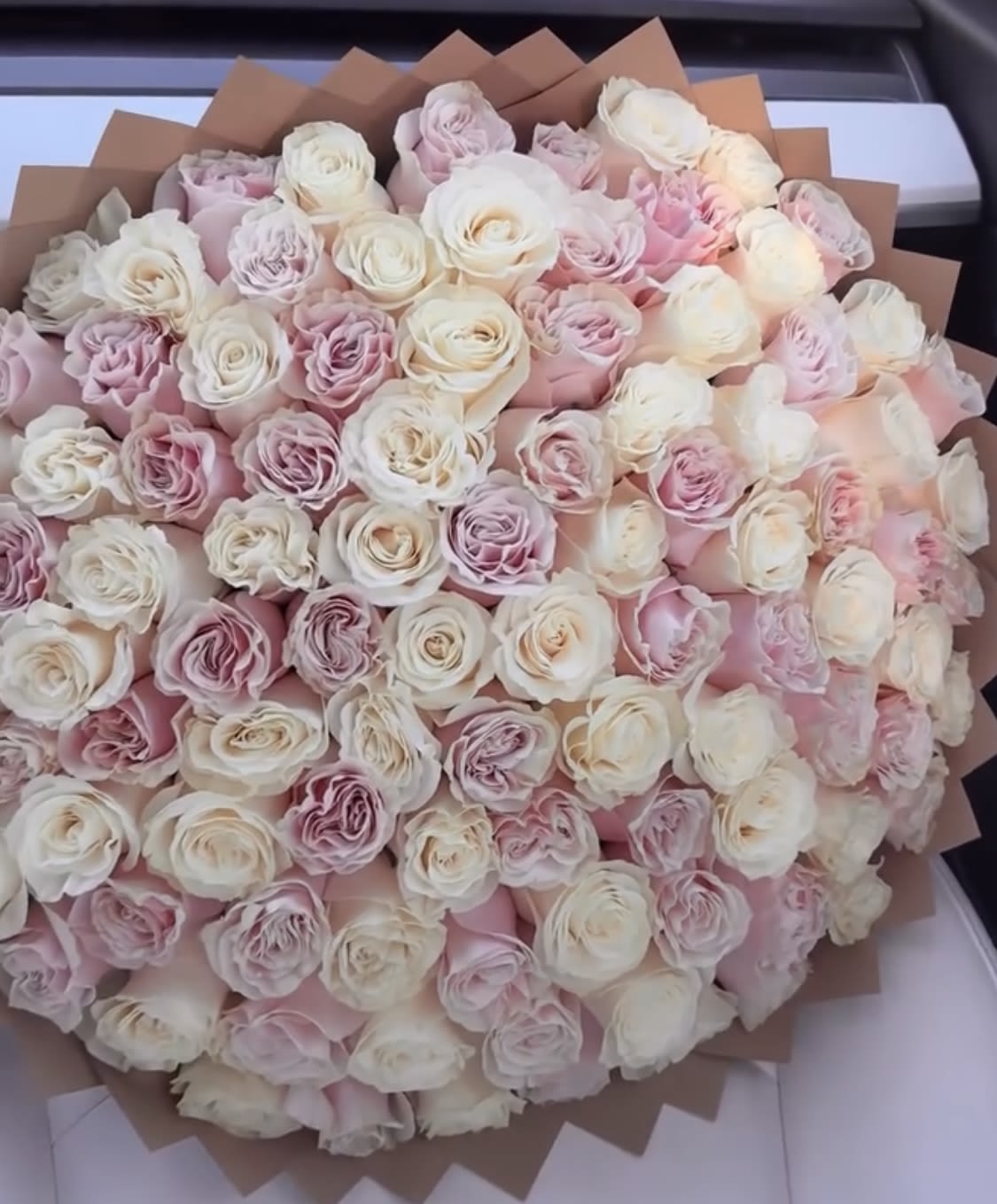 Large bouquet of pale pink and white roses wrapped in brown paper