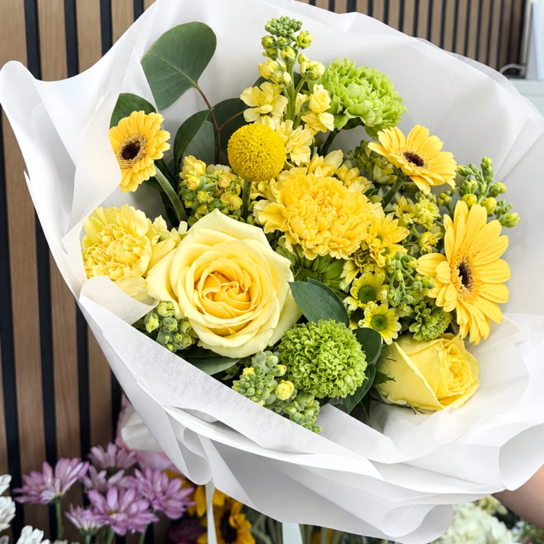 Yellow bouquet with roses, gerbera daisies, and green blooms wrapped in white paper