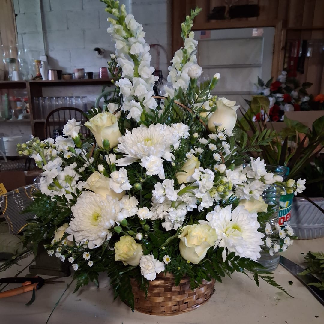 White floral arrangement in a woven basket with roses and tall snapdragons
