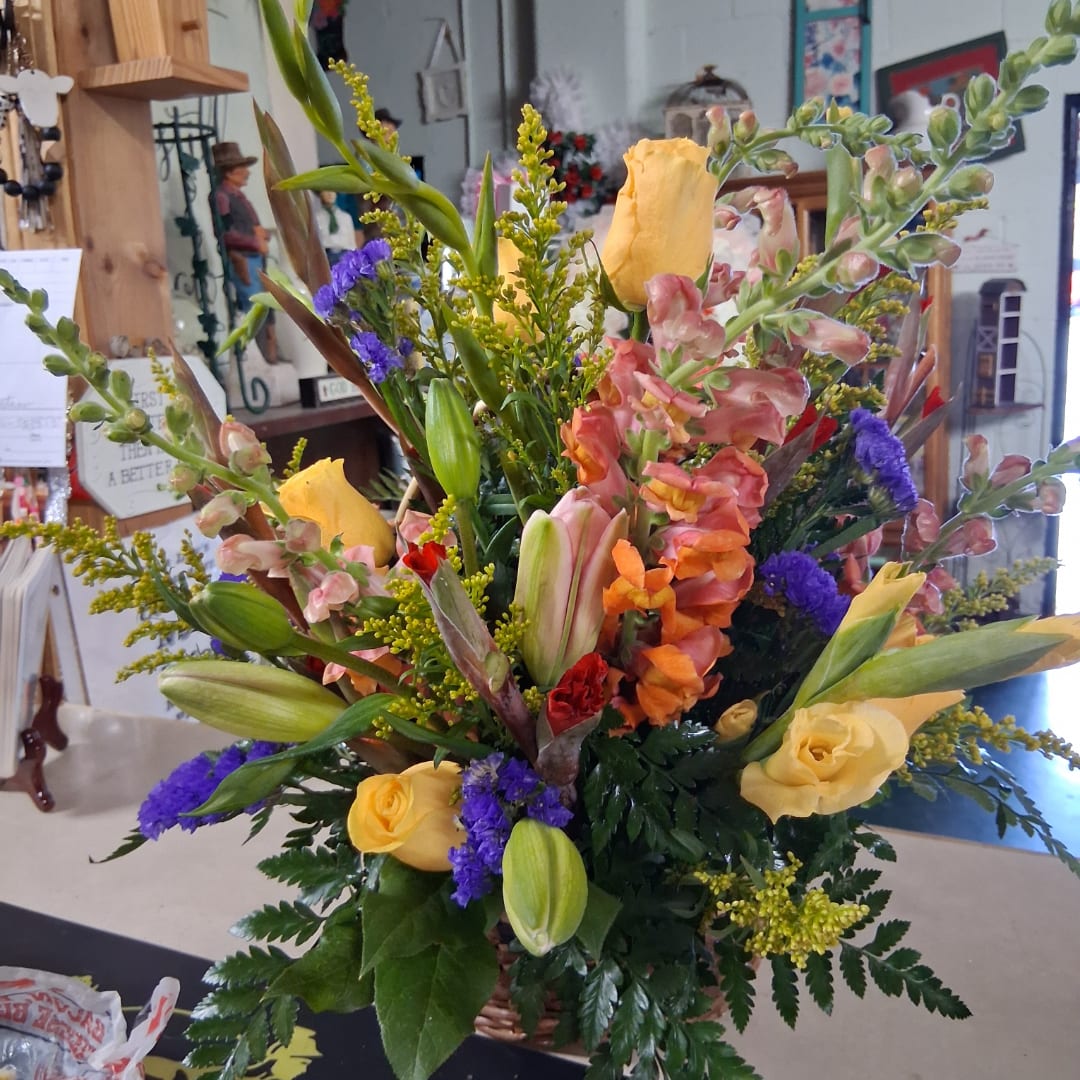 Mixed bouquet with yellow roses, lilies, and purple filler flowers in a basket