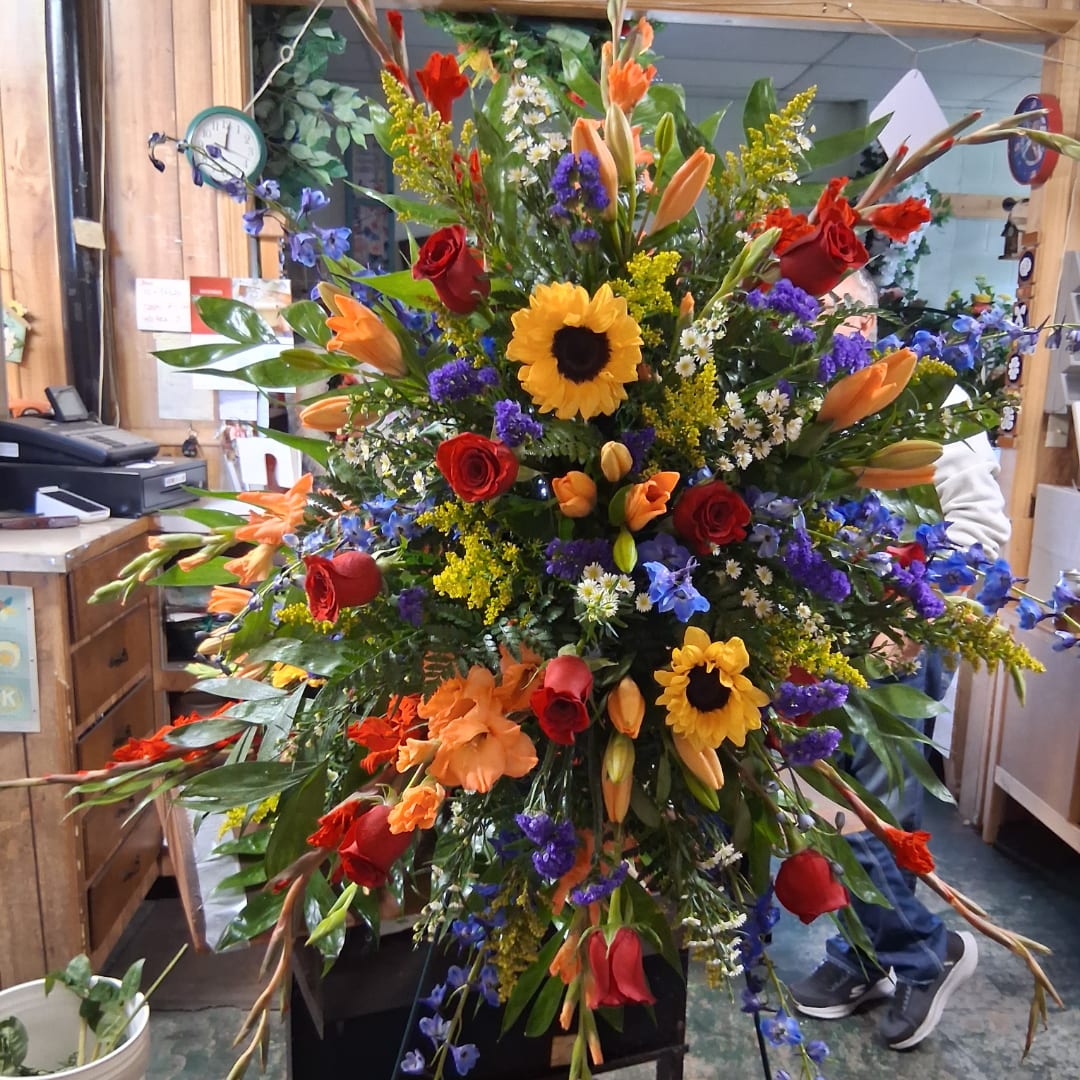 Large mixed floral spray with sunflowers, roses, lilies, and blue accents