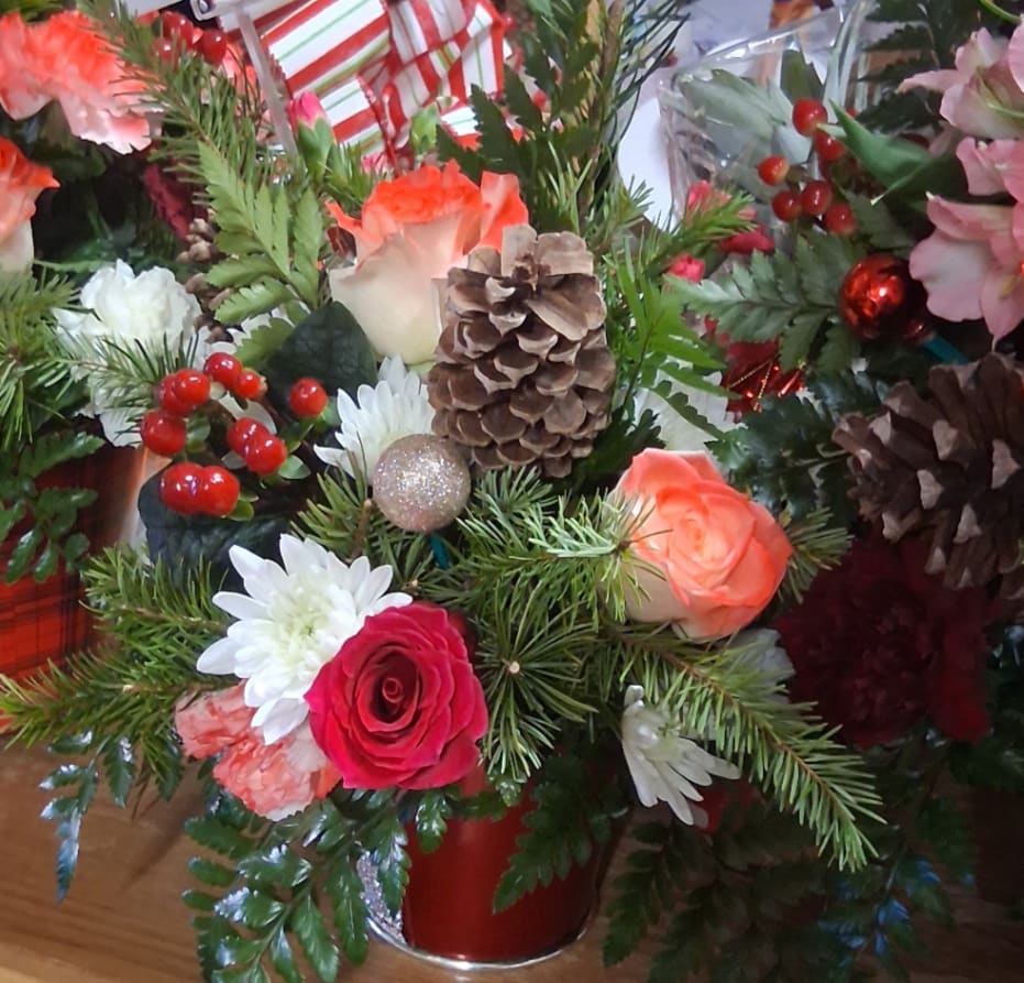Holiday floral arrangement with roses, daisies, pinecones, and red berries in a red vase