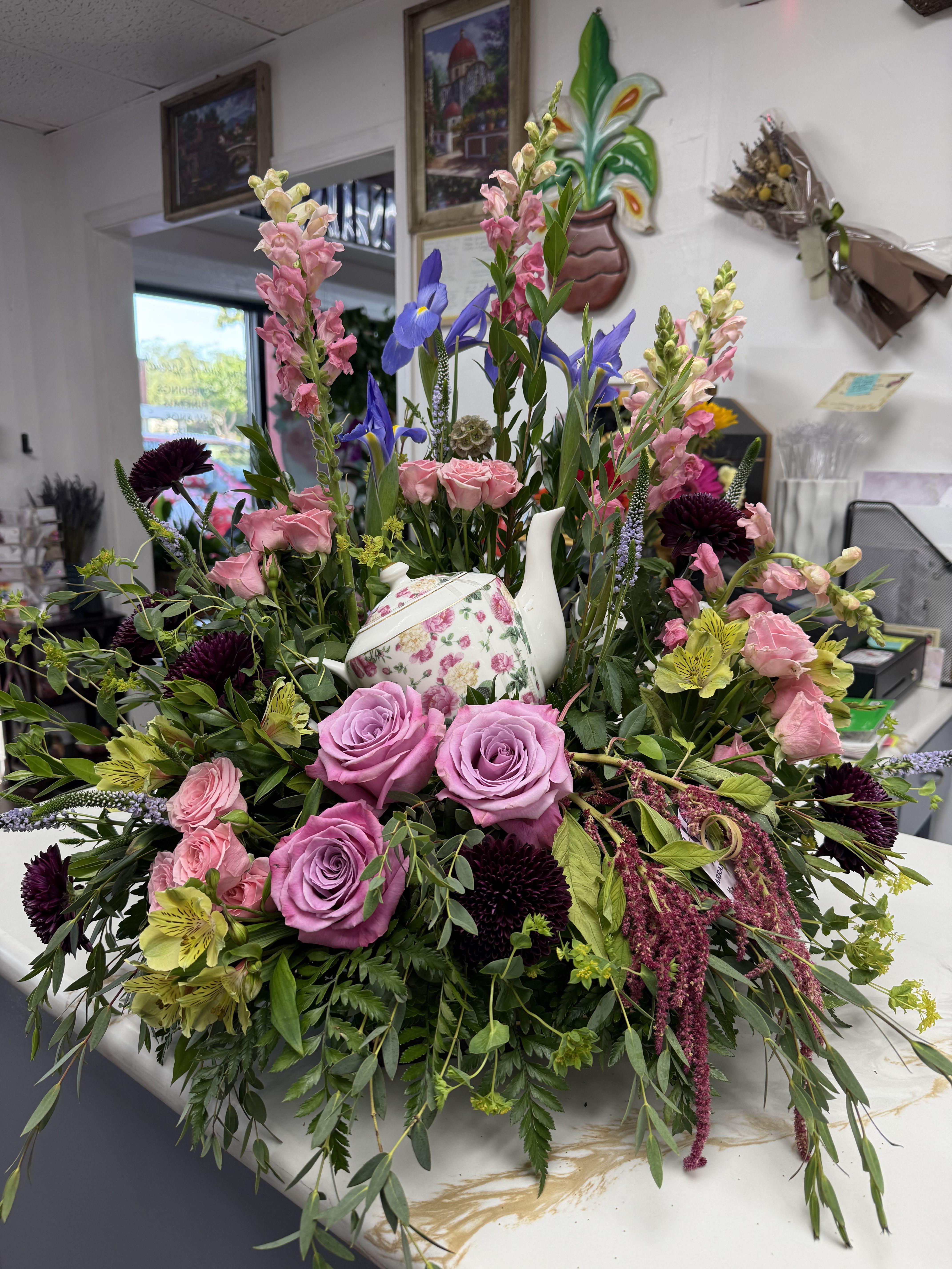 Mixed floral arrangement with roses, snapdragons, and a floral teapot centerpiece