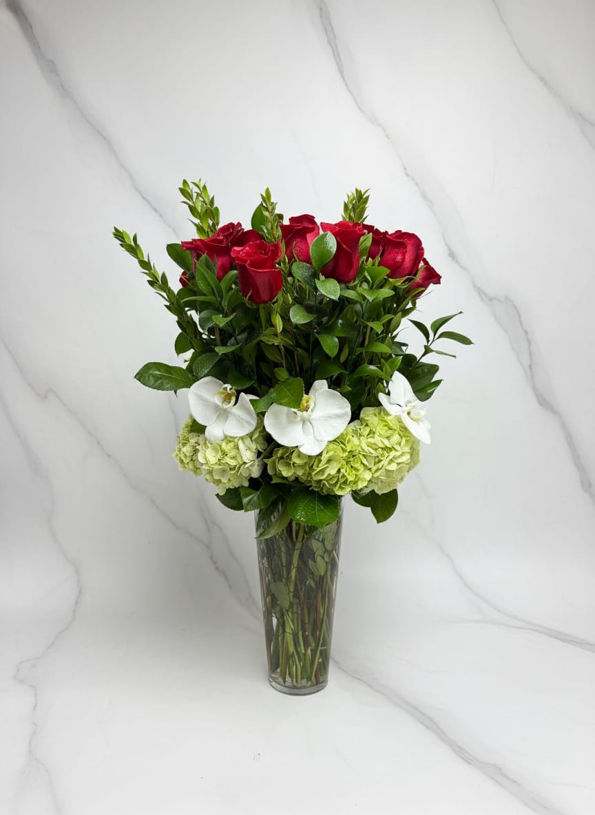 Red roses and white orchids arranged in a tall glass vase