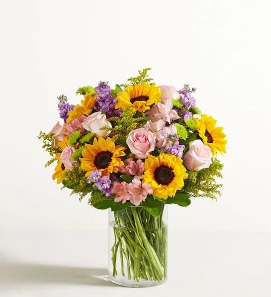 Bouquet of sunflowers, pink roses, and purple flowers in a glass vase