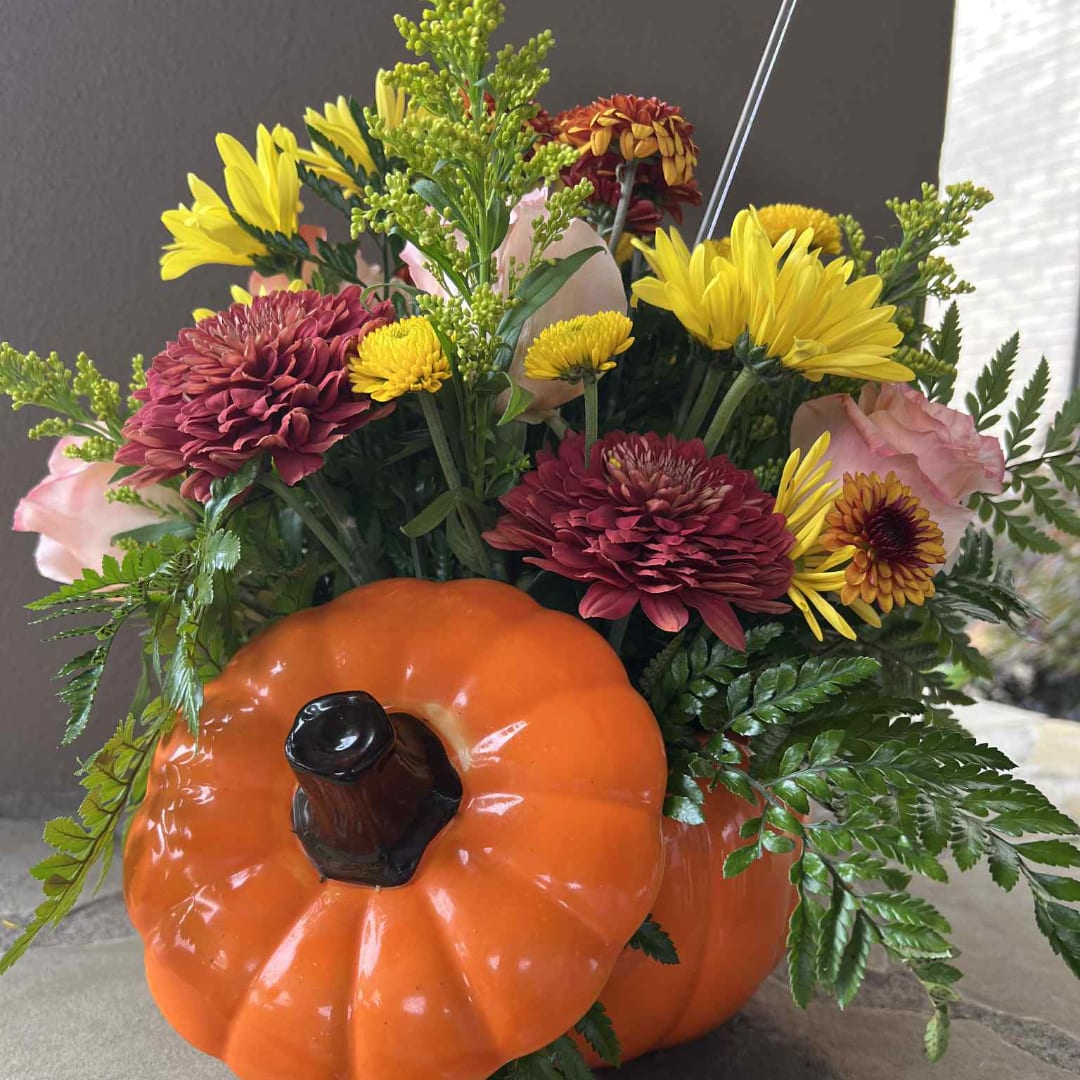 Flowers arranged in a pumpkin-shaped container with yellow and burgundy blooms
