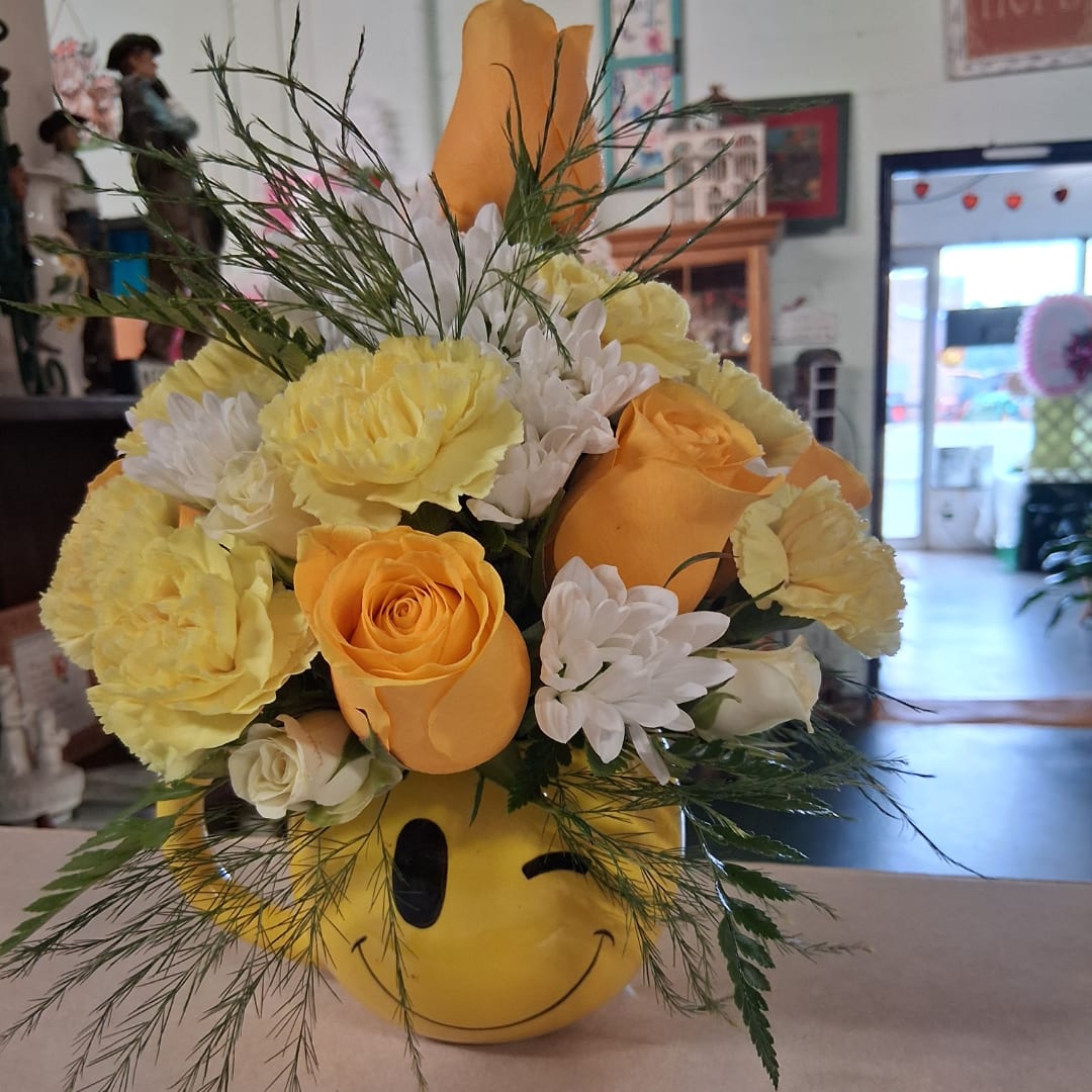 Yellow and white flower arrangement in a smiley-face container