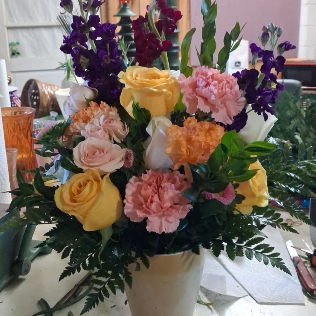 Mixed bouquet of roses, carnations, and purple flowers in a white vase