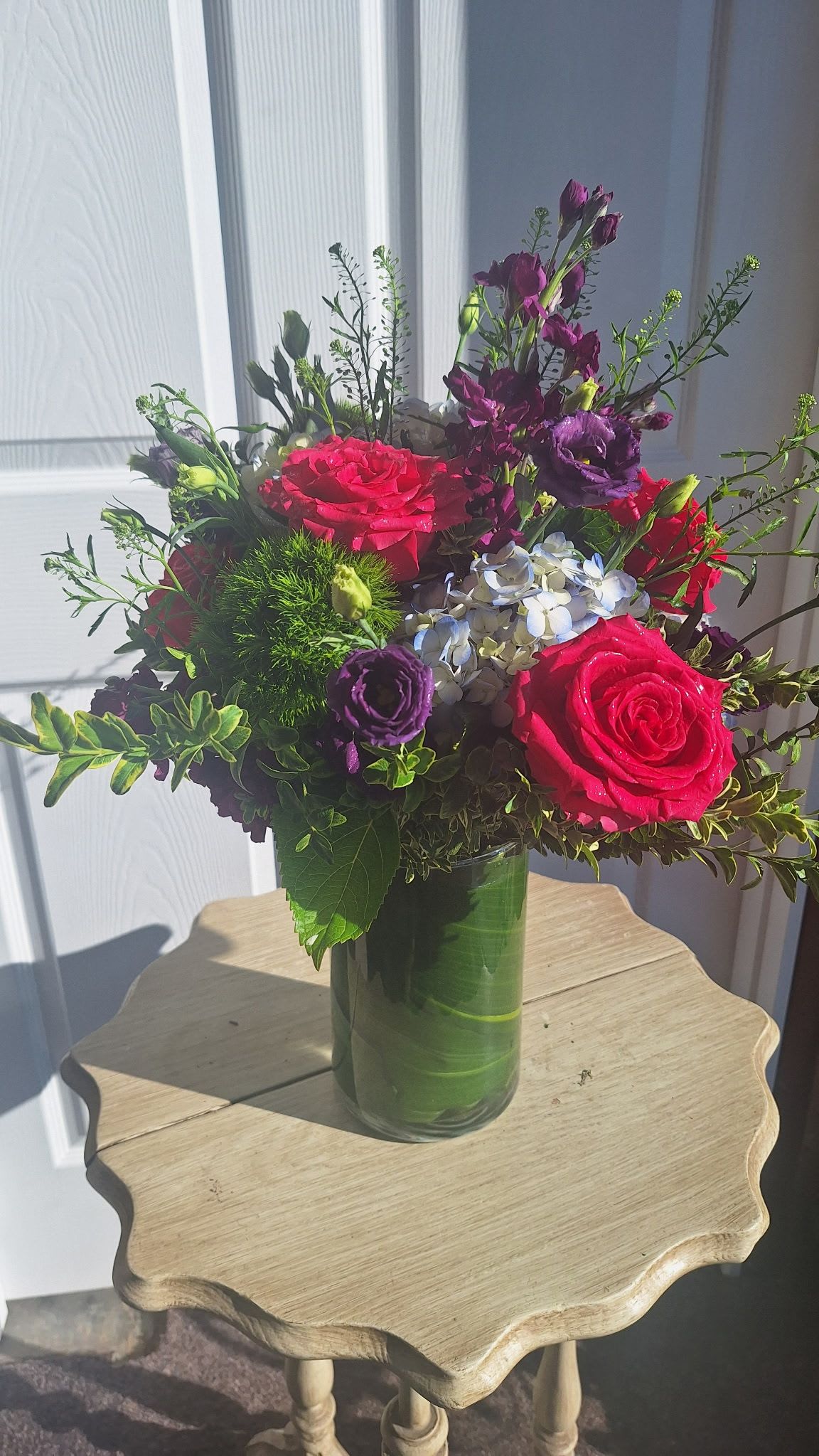 Vibrant arrangement of hot pink roses, purple flowers, and hydrangea in a clear glass vase.