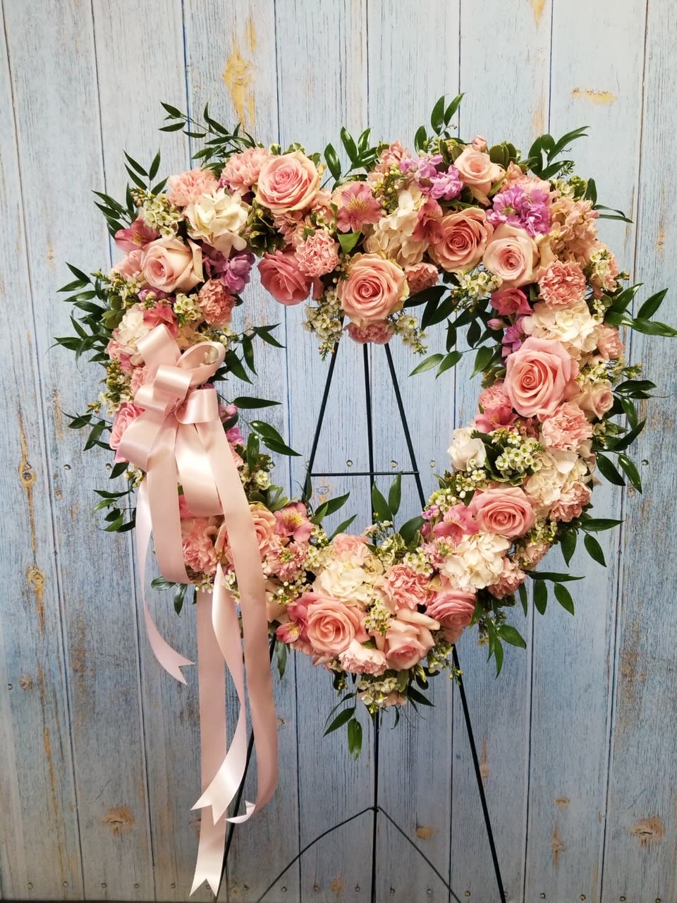 Heart-shaped floral wreath with pink roses and a satin ribbon on a stand