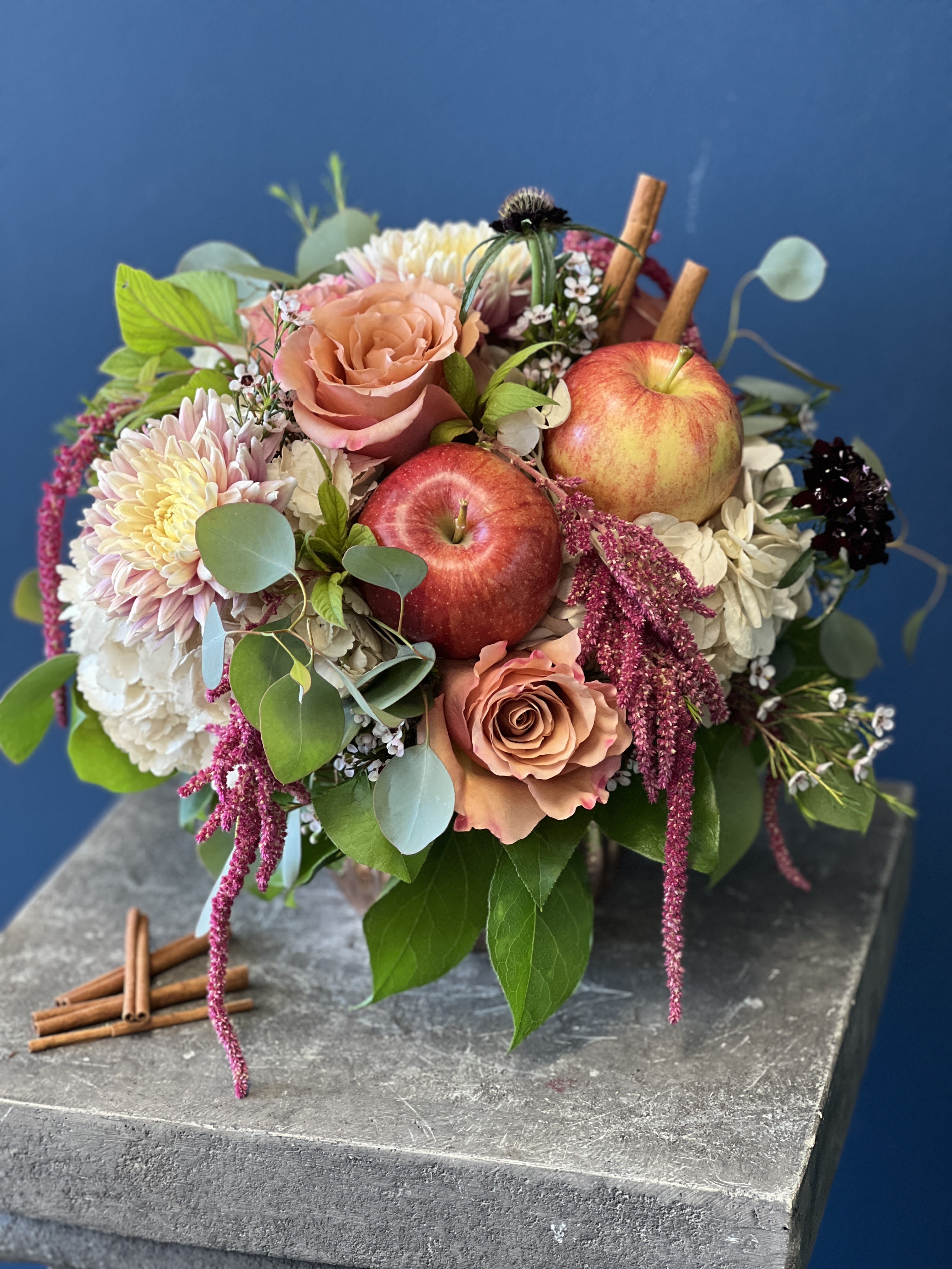 Mixed bouquet with roses, chrysanthemums, and apples on a stone pedestal