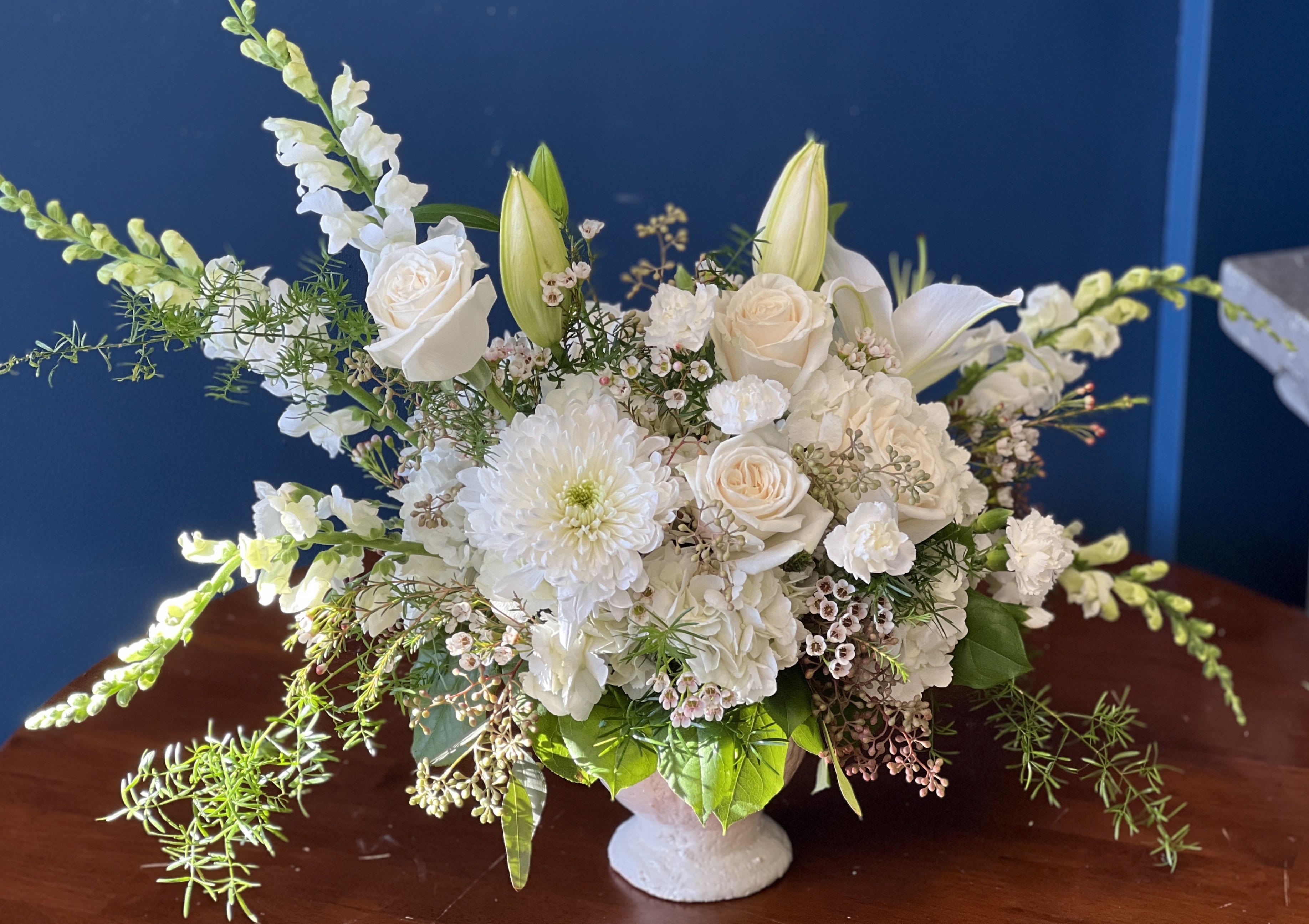 White floral arrangement in a white vase with roses, lilies, and chrysanthemums