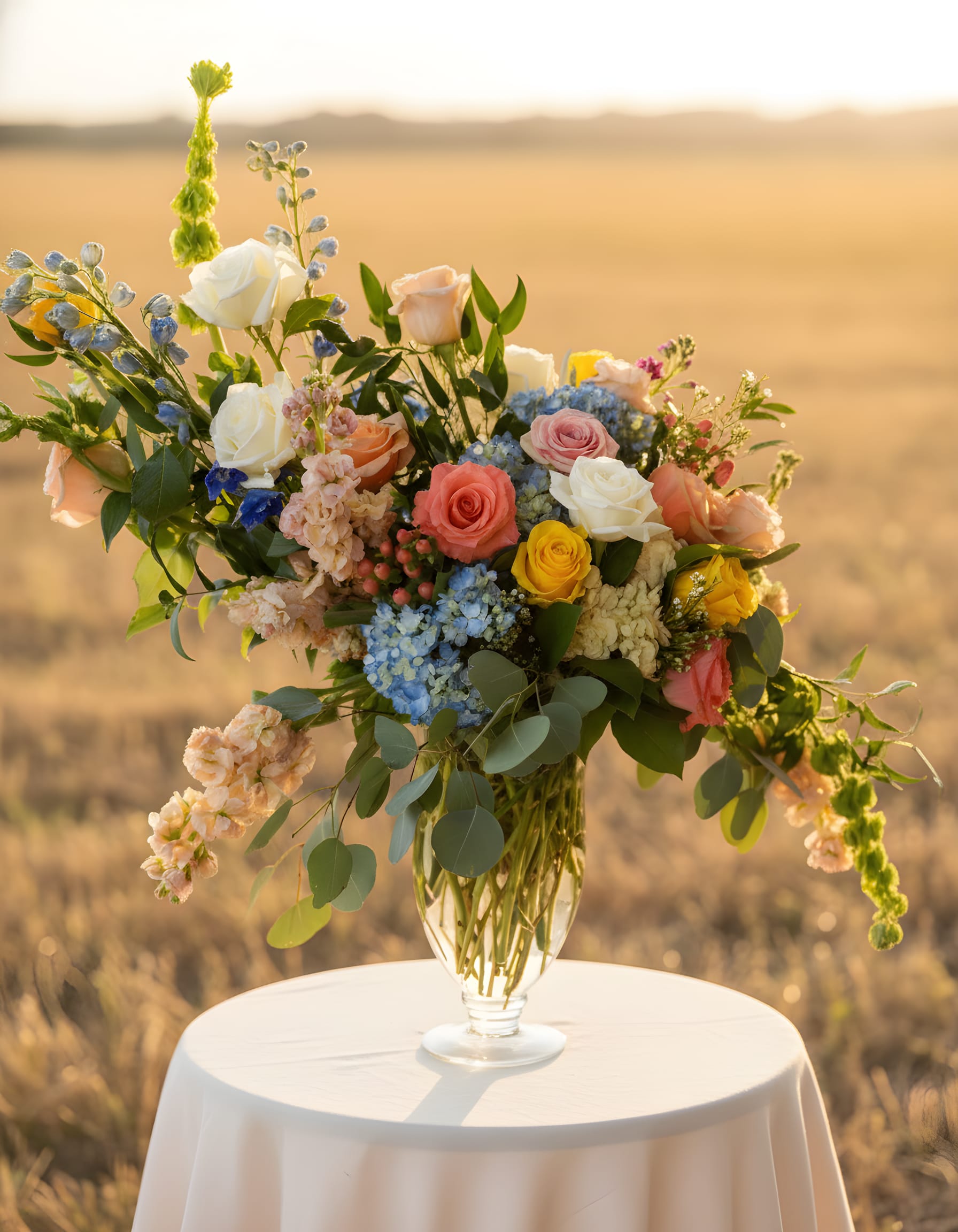 Mixed roses and blue flowers in a clear glass vase on a round table