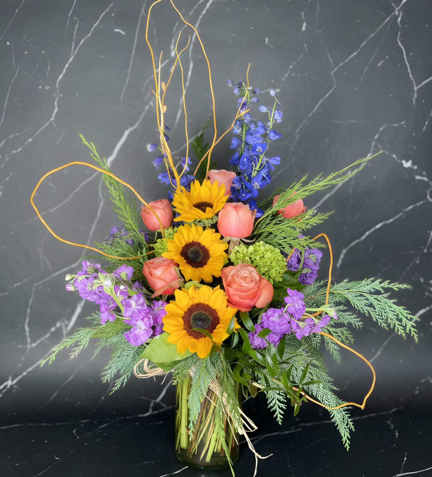 Bouquet of sunflowers, pink roses, and purple flowers in a glass vase