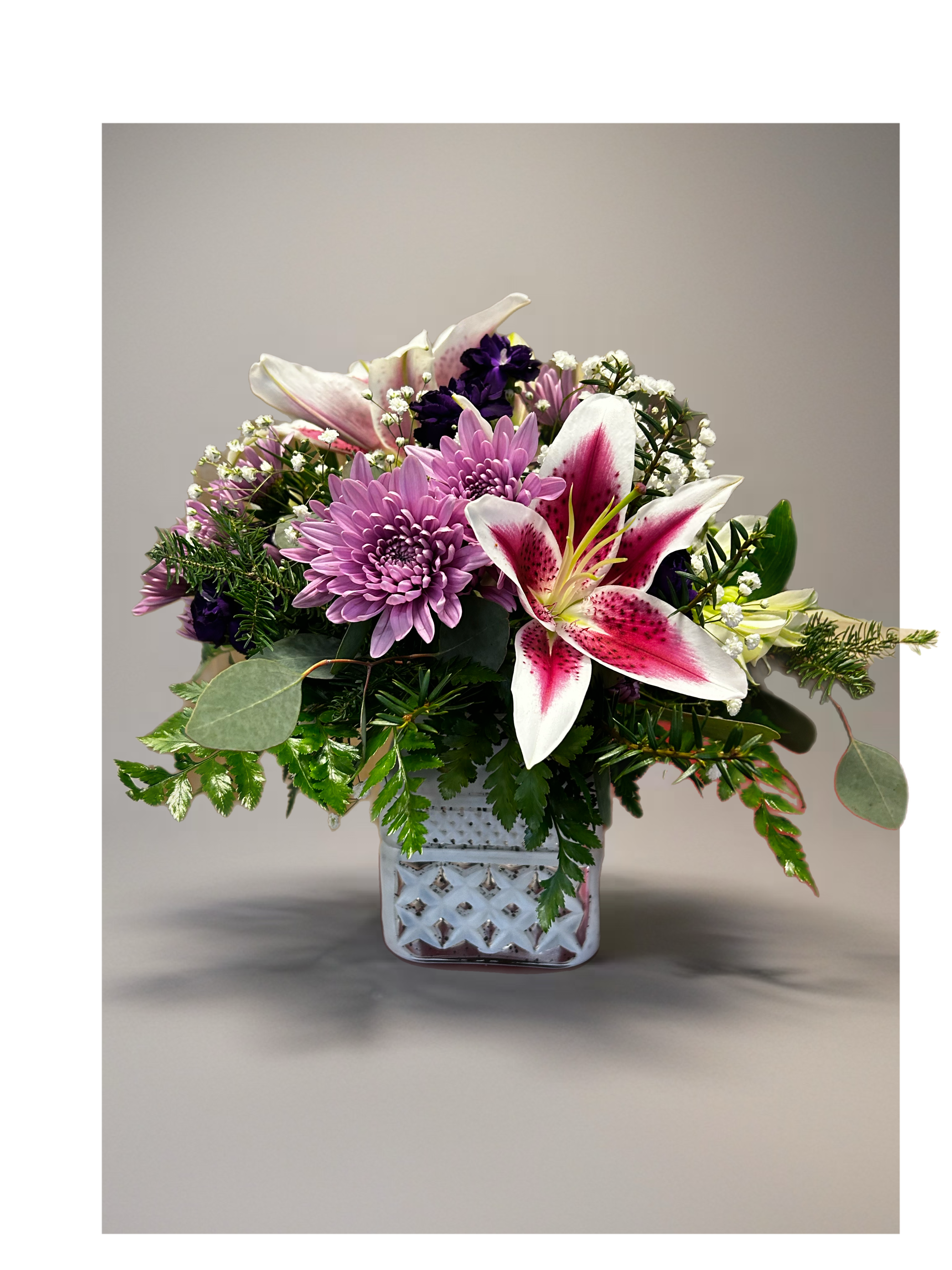 Pink lilies and lavender mums arranged with white filler flowers in a white cube vase