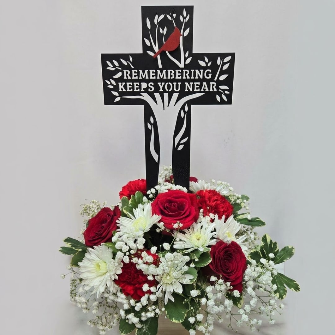 Red and white sympathy arrangement beneath a memorial cross sign