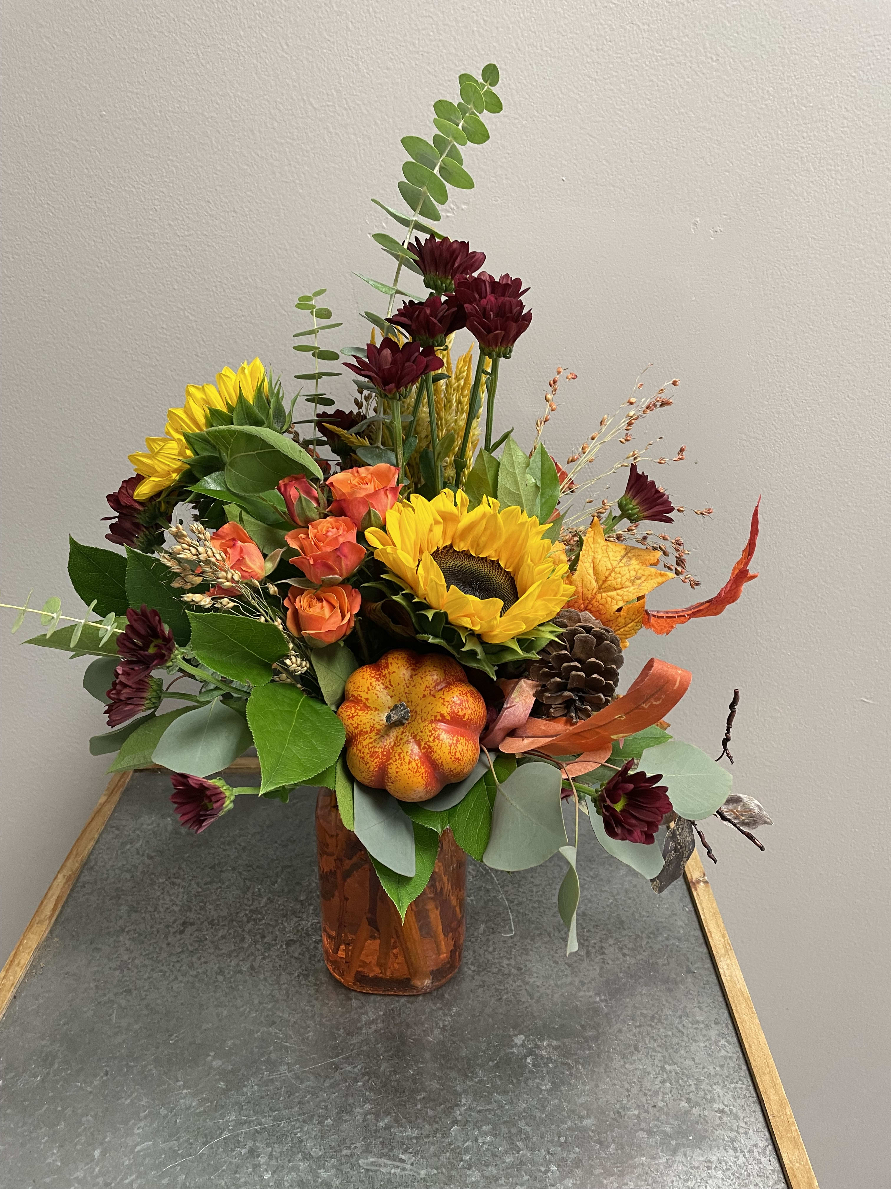 Festive Fall Fun - Brighten up someone's day with this beautiful and bright fall arrangement. This fall vase is filled with sunflowers, miniature roses, mums, and assorted fall foliage and fillers. To add more fall flare, it has a pumpkin pick added in. This is the perfect vase to have on your table to welcome the crisp fall days.