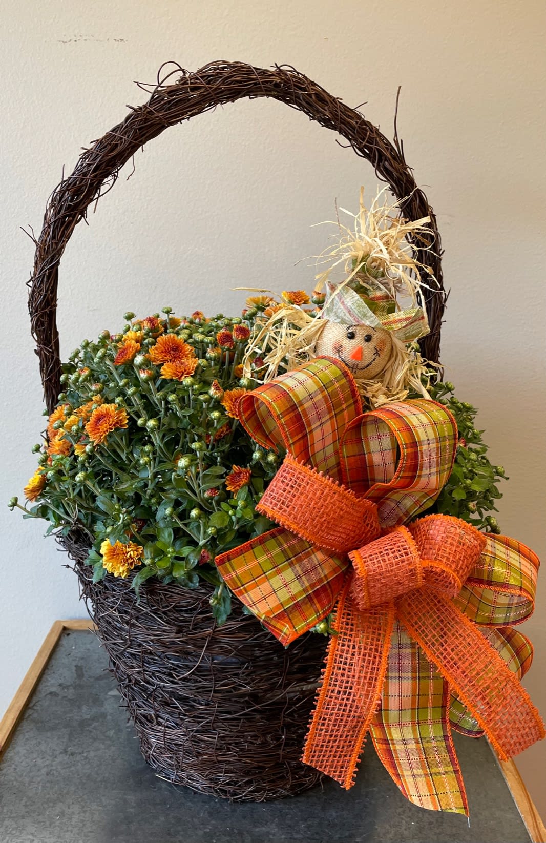 Cheerful Mums - This rustic basket is filled with a bright and festive hardy mum to add some fall cheer to any porch or deck! The scarecrow pick and fall ribbon add bright festive touches to make this the perfect gift for any occasion! *Mum colors and scarecrows may vary from each order. If you prefer a certain color, please let us know in the special instructions and we will try our best to get the color for you.